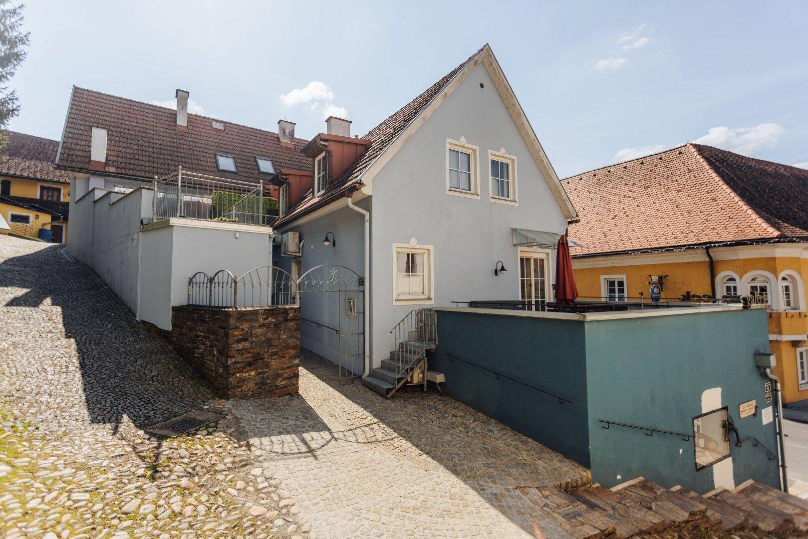 Ansicht des Gebäudes von oben, mit seitlichem Zugang, Terrasse und gepflasterter Auffahrt.