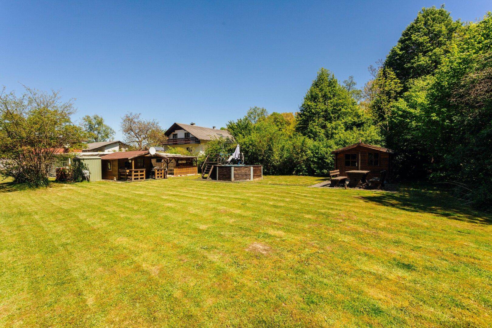 Weitläufiger Garten mit Rasenfläche, einem Holzschuppen und einem Aufstellpool im Hintergrund.