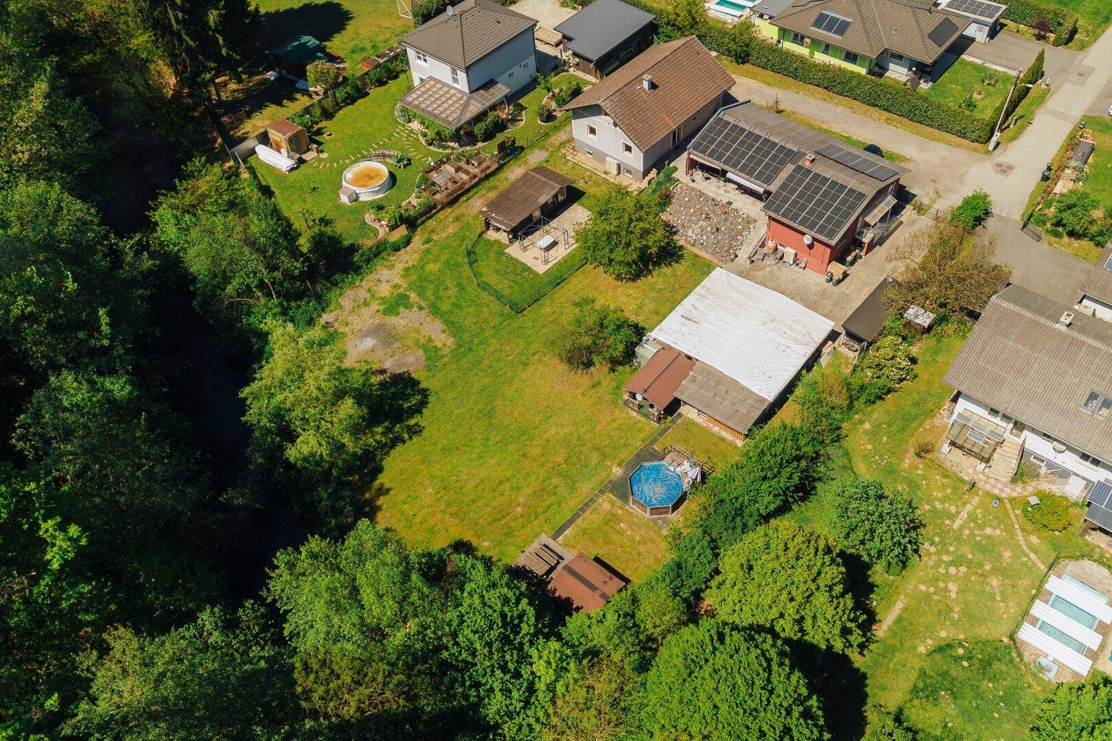 Vogelperspektive des Grundstücks mit großem Garten, Pool und angrenzendem Waldgebiet.