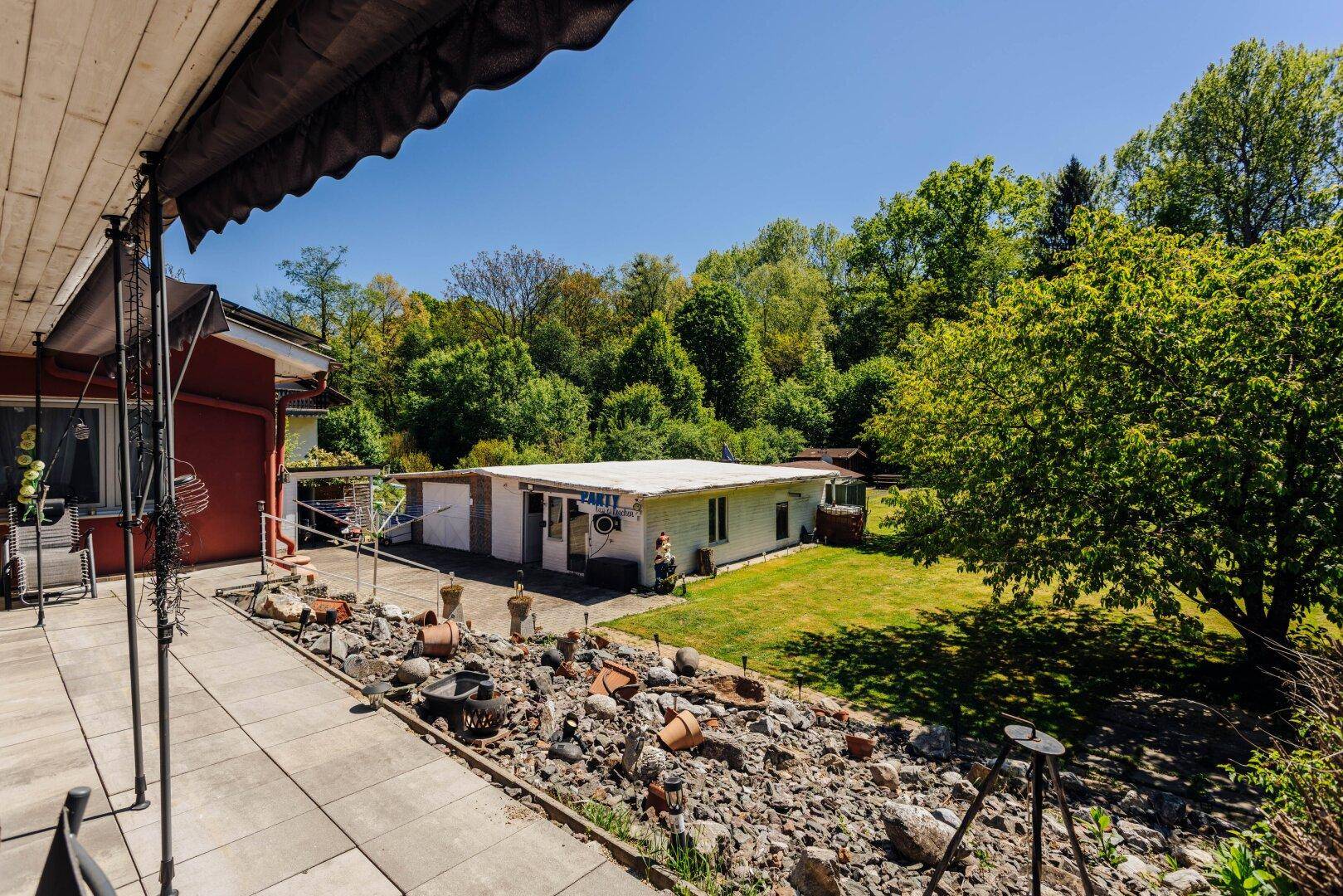 Überdachte Terrasse mit Fliesenboden, Gartenmöbeln und Blick auf den Garten und das Nebengebäude.