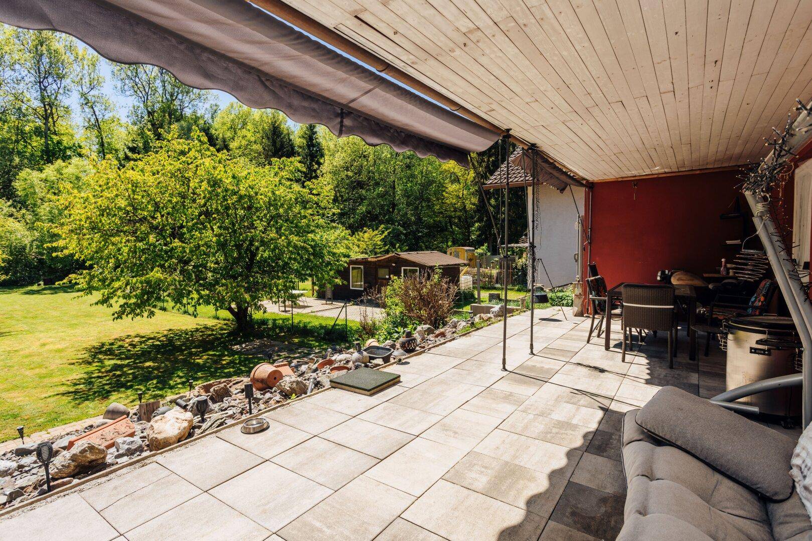 Überdachte Terrasse mit Fliesenboden, bequemen Gartenmöbeln und Blick auf den grünen Garten.