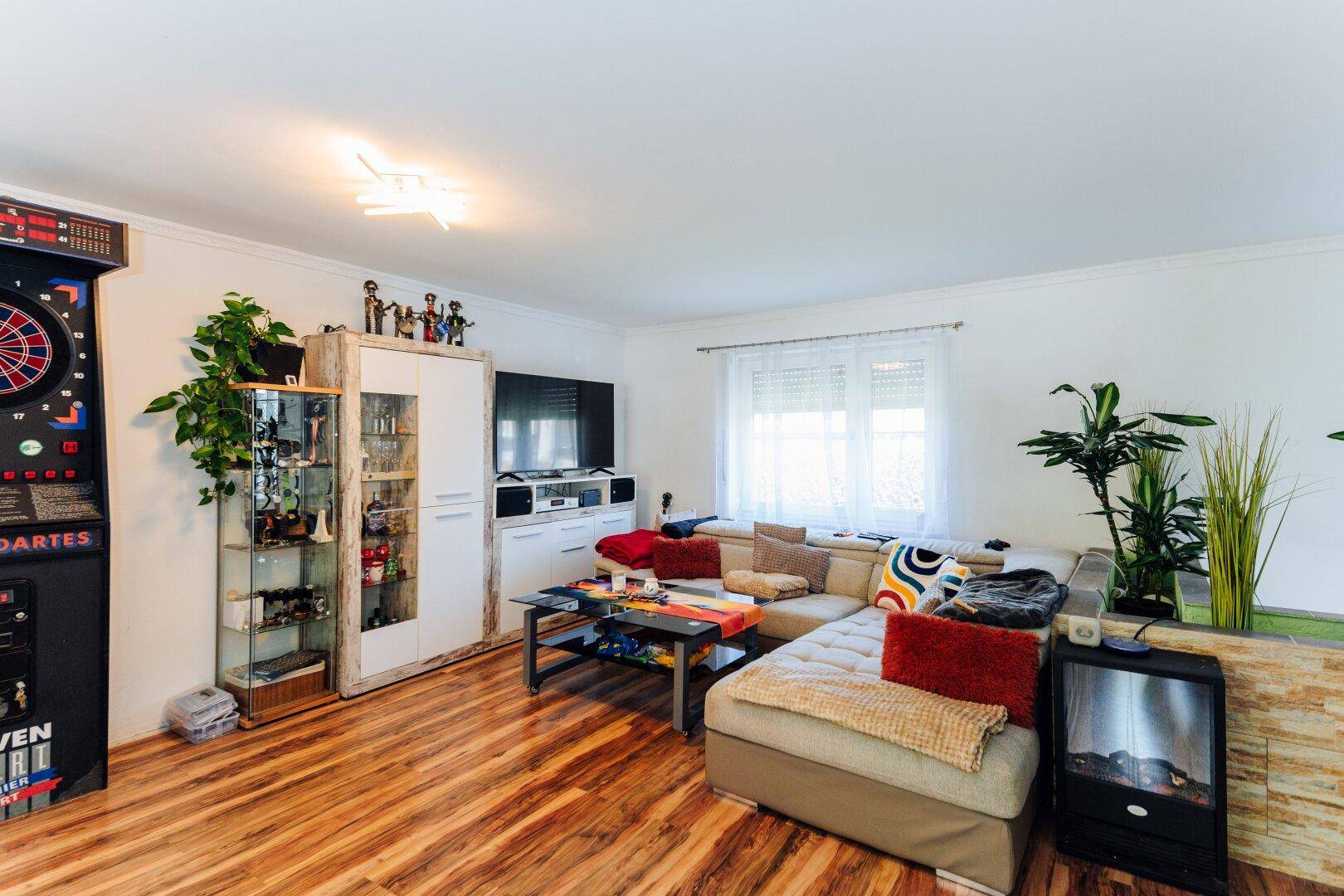 Gemütliches Wohnzimmer mit großem Ecksofa, Fernseher, Pflanzen und Laminatboden.