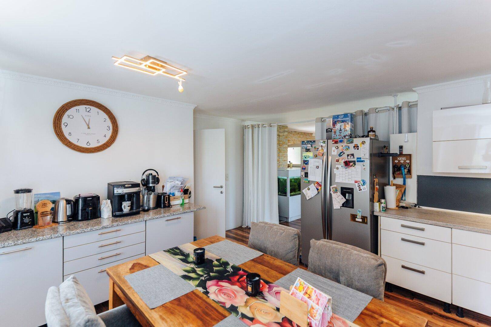 Essbereich und Küche mit Holztisch, weißen Schränken und großem Kühlschrank.