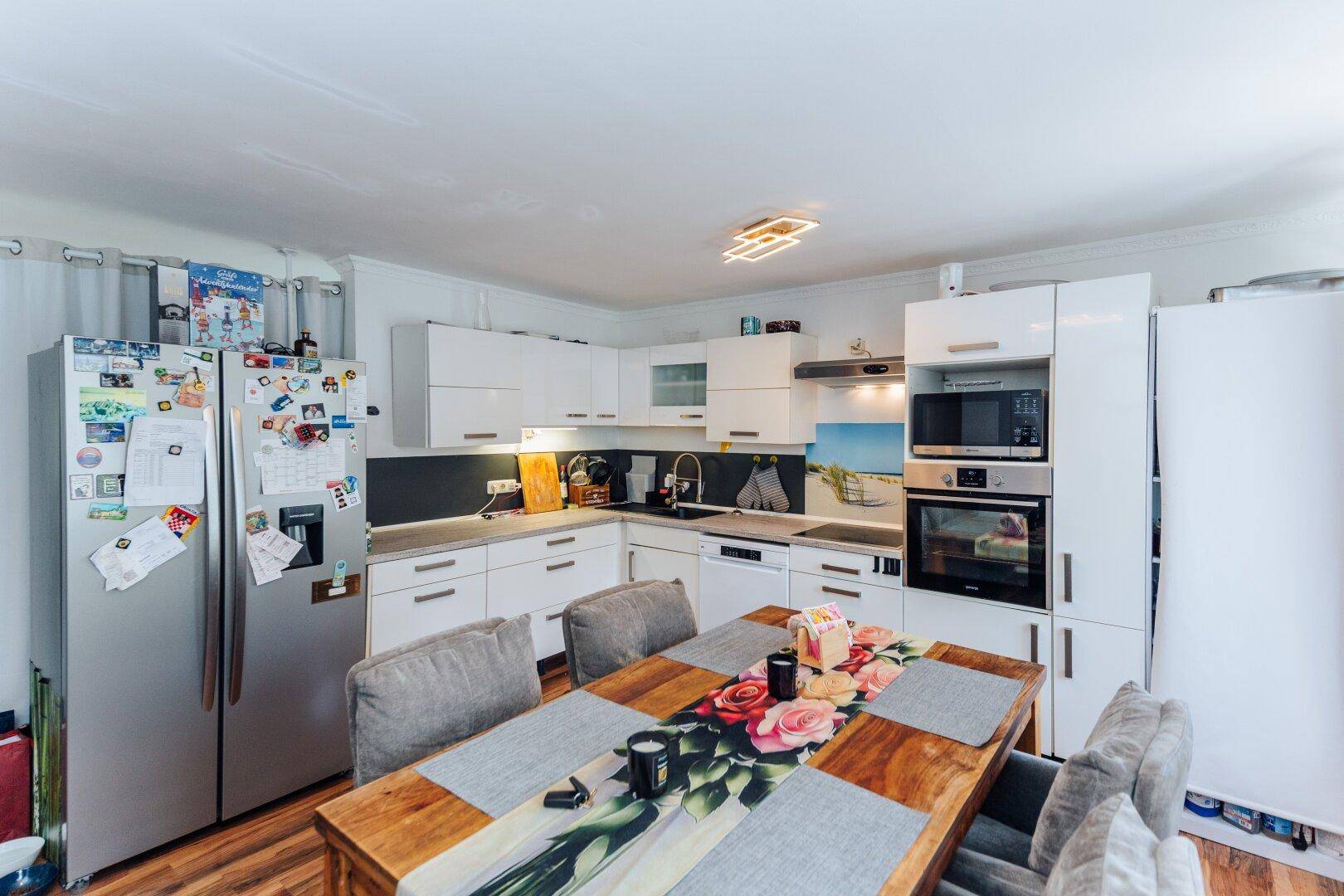 Moderne Küche mit weißen Schränken, Einbaugeräten, Esstisch und großem Kühlschrank.