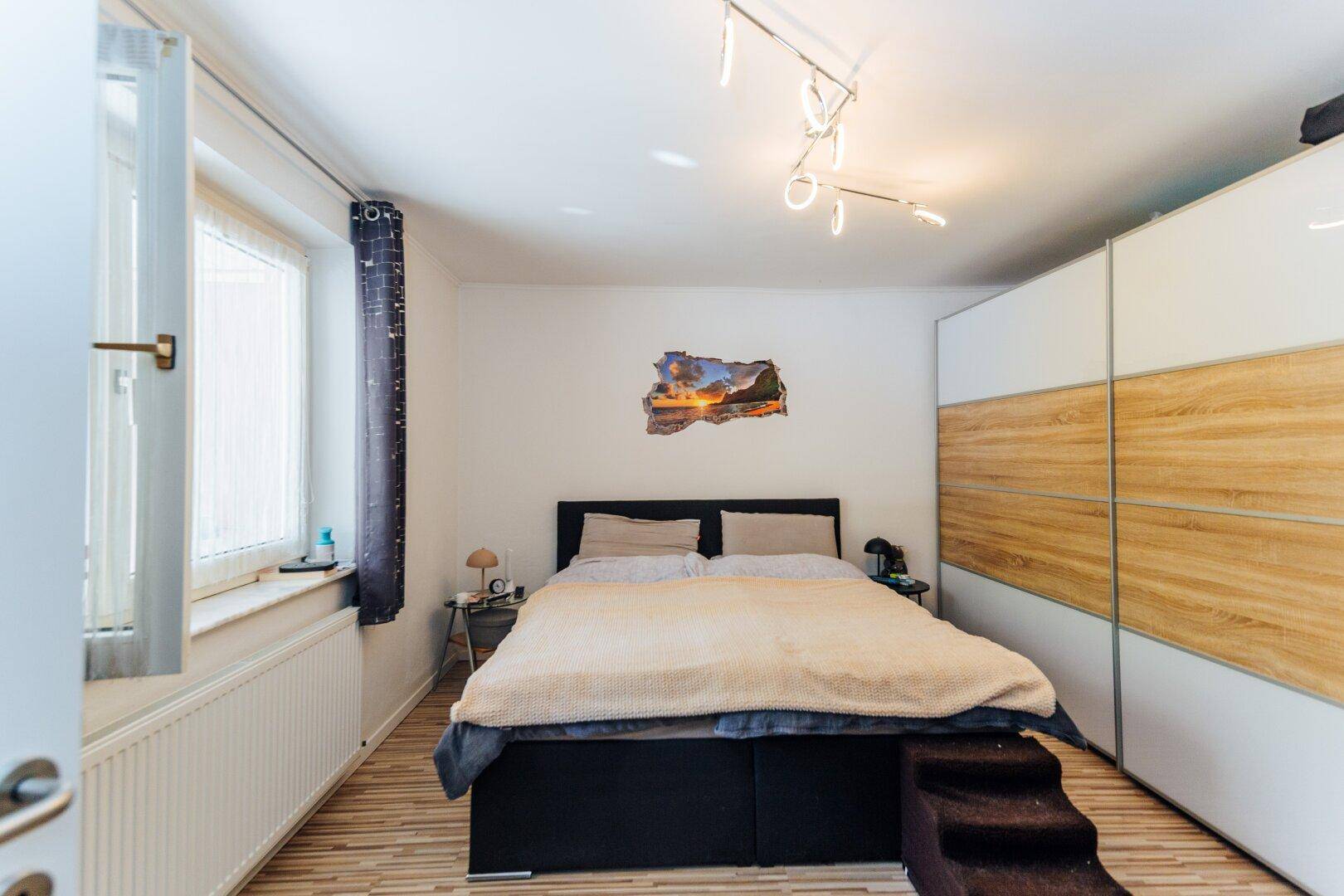 Helles Schlafzimmer mit Doppelbett, Laminatboden und einem großen Kleiderschrank mit Holzfronten.