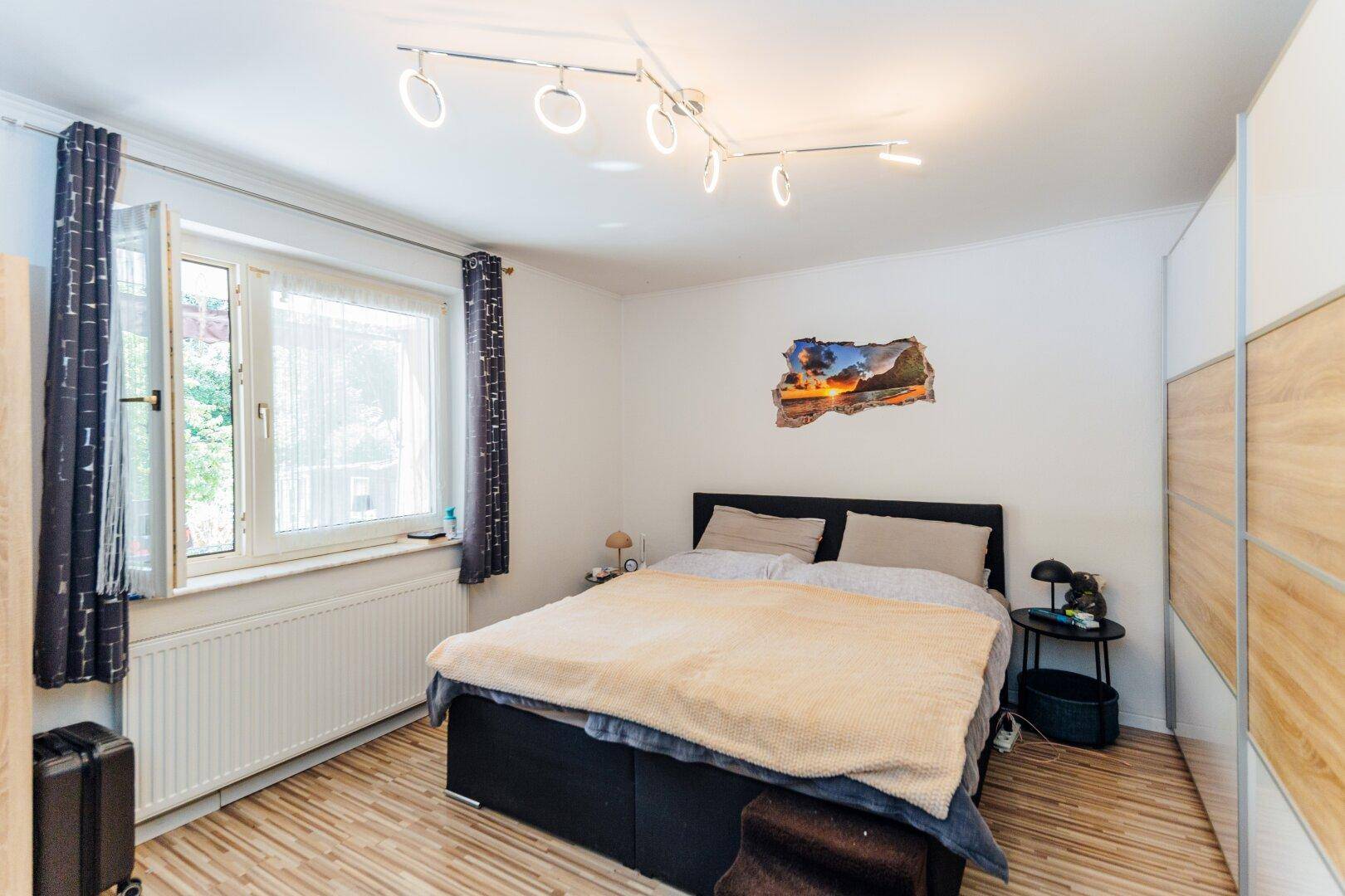 Schlafzimmer mit großem Fenster, Laminatboden und einem geräumigen Kleiderschrank für viel Stauraum.