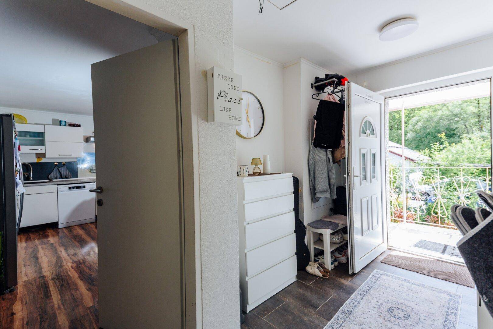Eingangsbereich mit Holzboden, Garderobe und Zugang zu einem kleinen Balkon mit Blick ins Grüne.