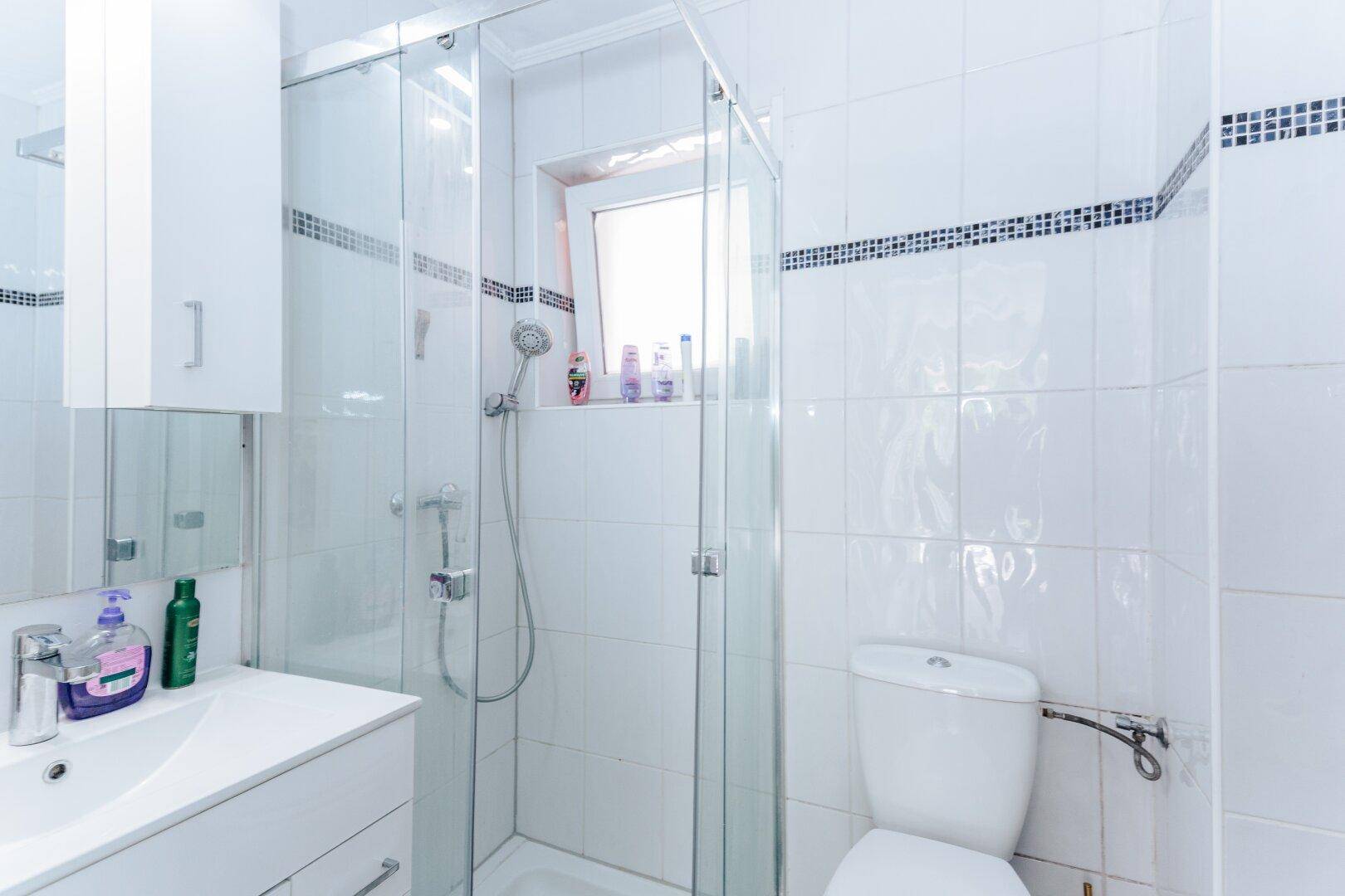 Kleines Badezimmer mit Duschkabine, WC und einem Fenster für natürliche Belüftung und Licht.