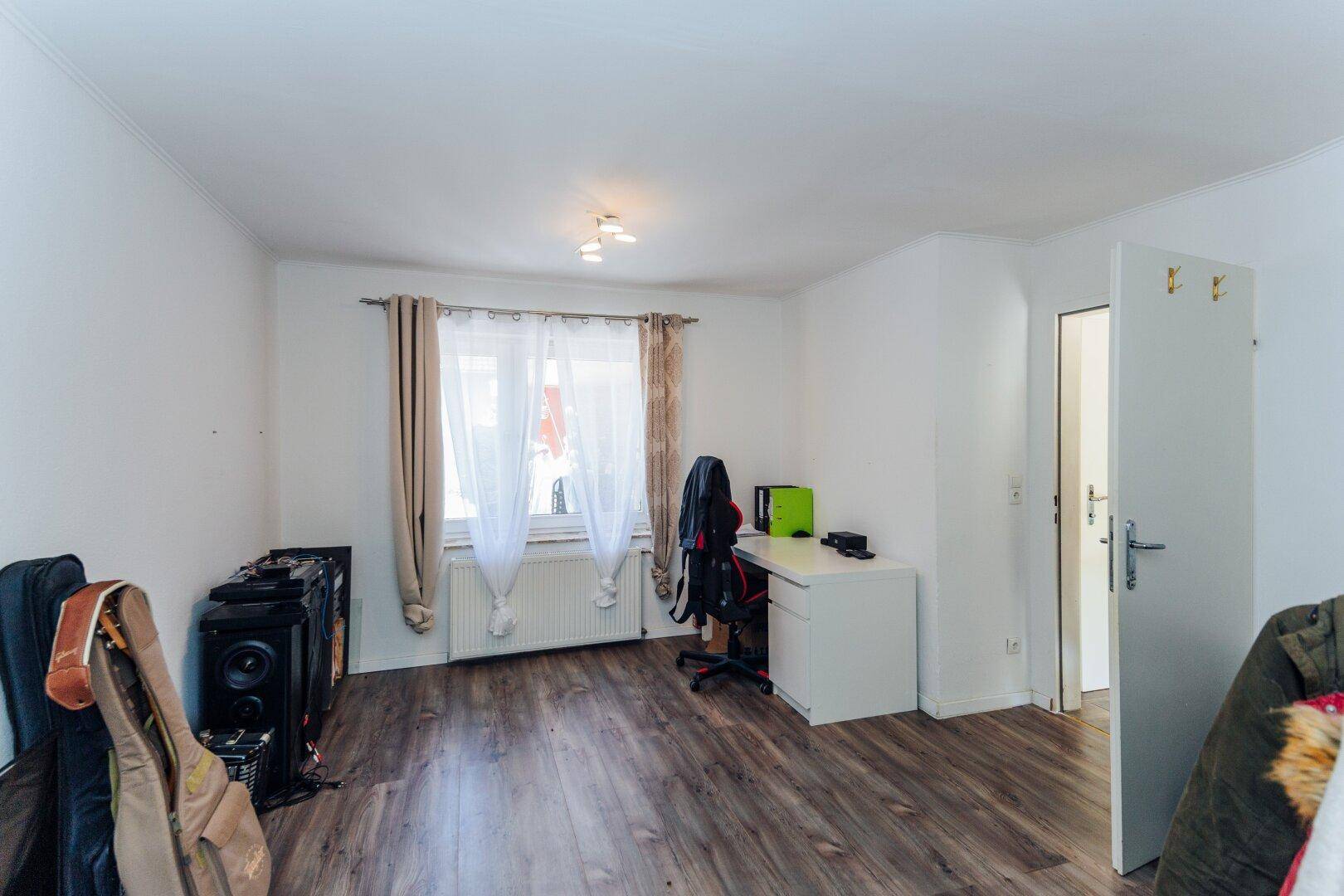 Geräumiges Zimmer mit Laminatboden, Schreibtisch und viel Platz für individuelle Gestaltungsmöglichkeiten.