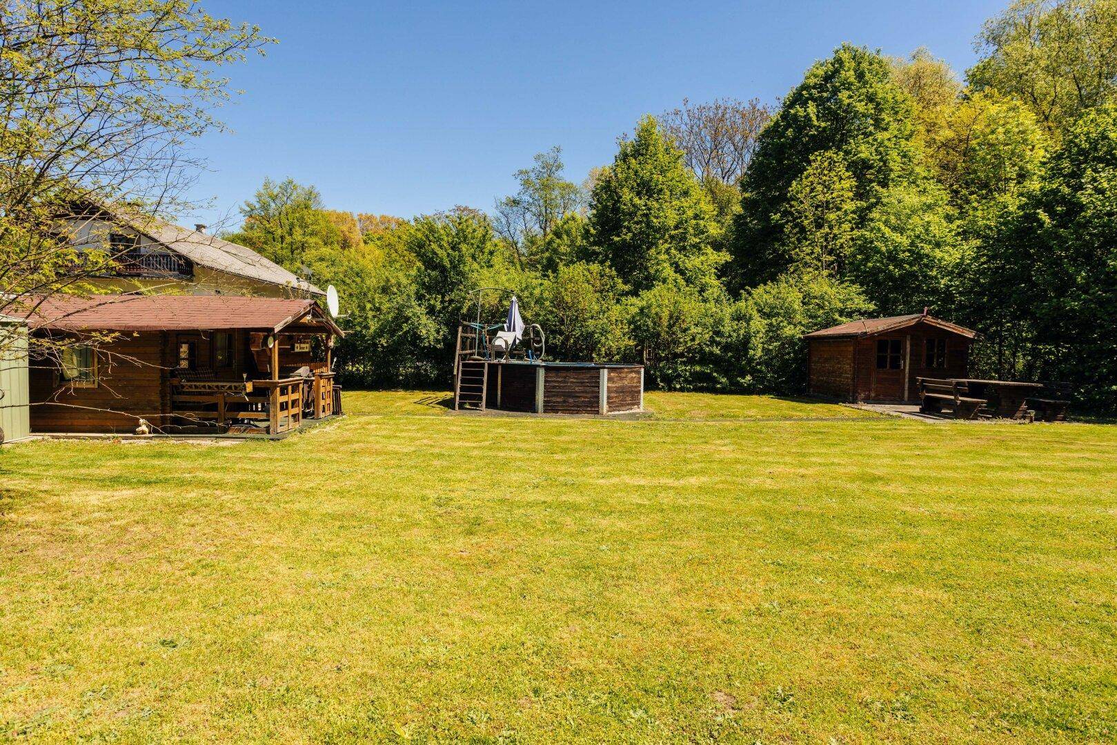 Großer Garten mit Rasen, einer Holzhütte, einem Aufstellpool und einem weiteren Schuppen.