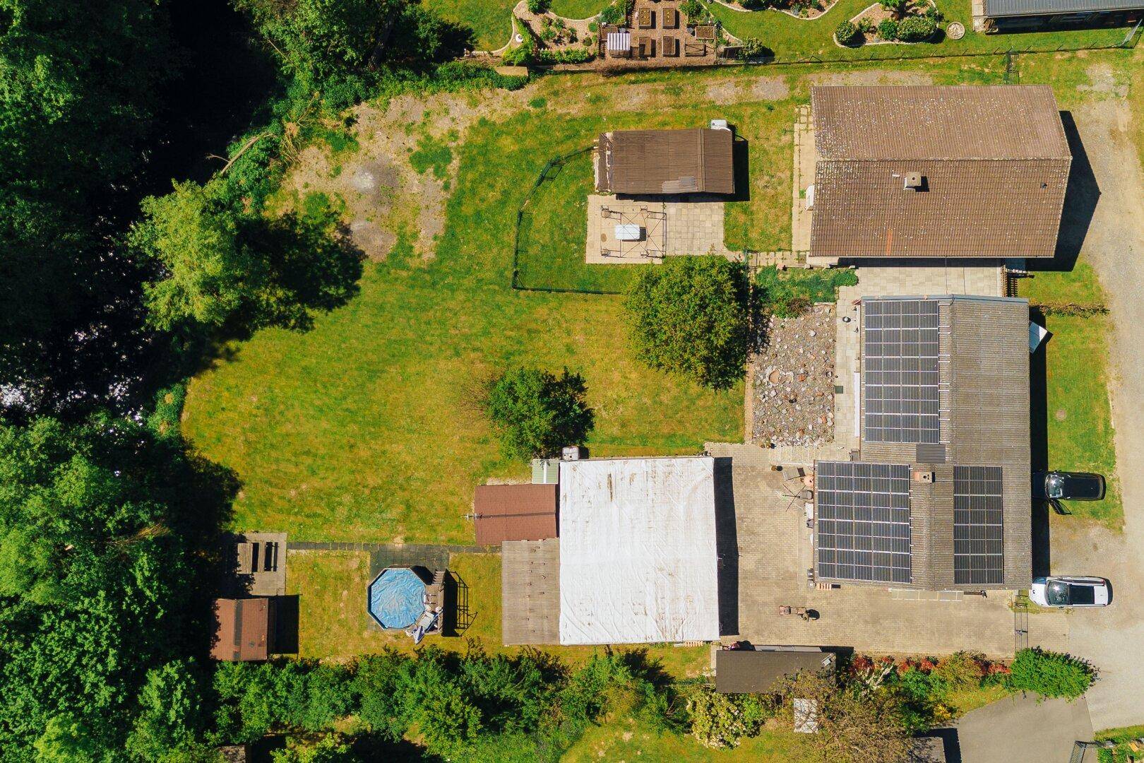 Detailansicht des Grundstücks von oben mit Solaranlagen, Pool und weitläufiger Rasenfläche.