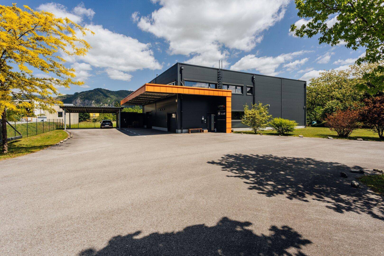 Außenansicht eines modernen Geschäftsgebäudes mit großem Parkplatz und grüner Umgebung.