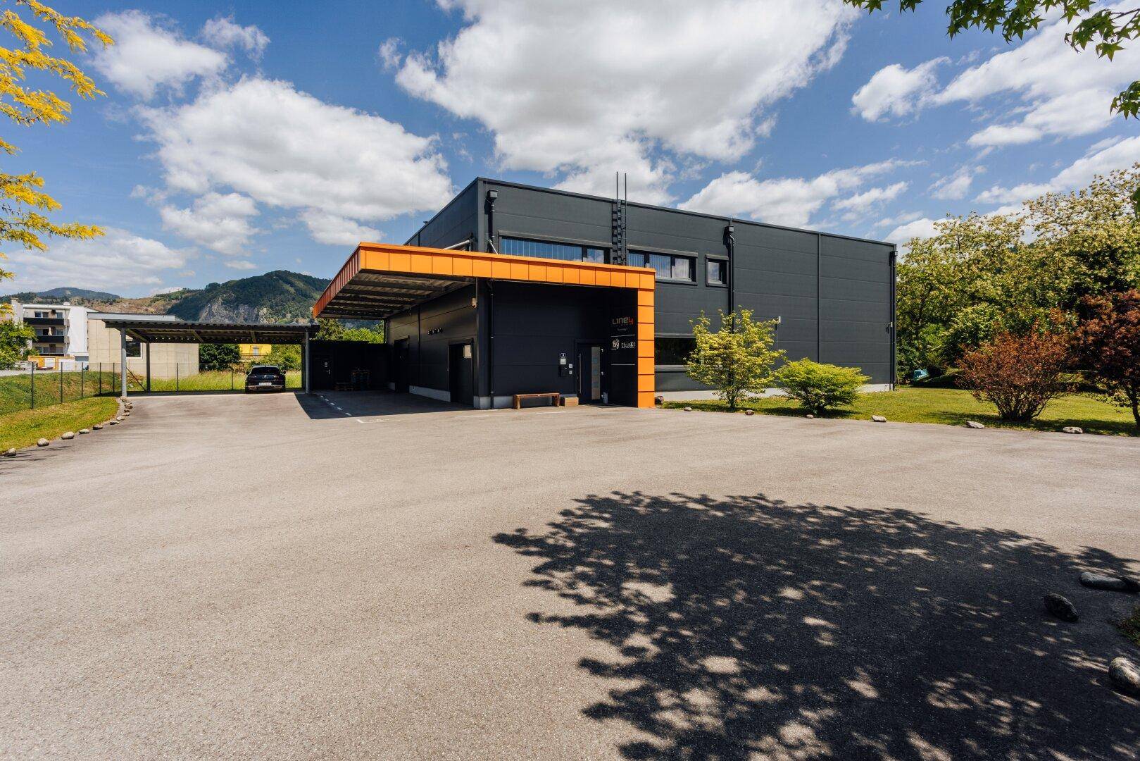 Modernes Geschäftsgebäude mit dunkler Fassade, orangefarbenen Akzenten und großem Parkplatz.