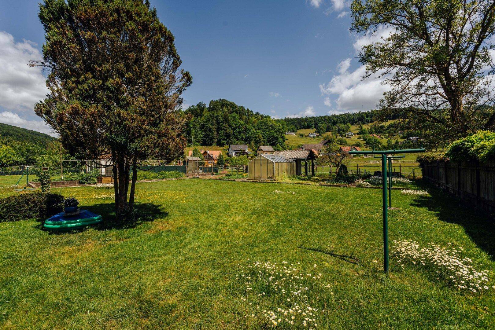 Weitläufiger Gartenbereich mit Wäscheleine, Gewächshaus und Blick auf die hügelige Landschaft.