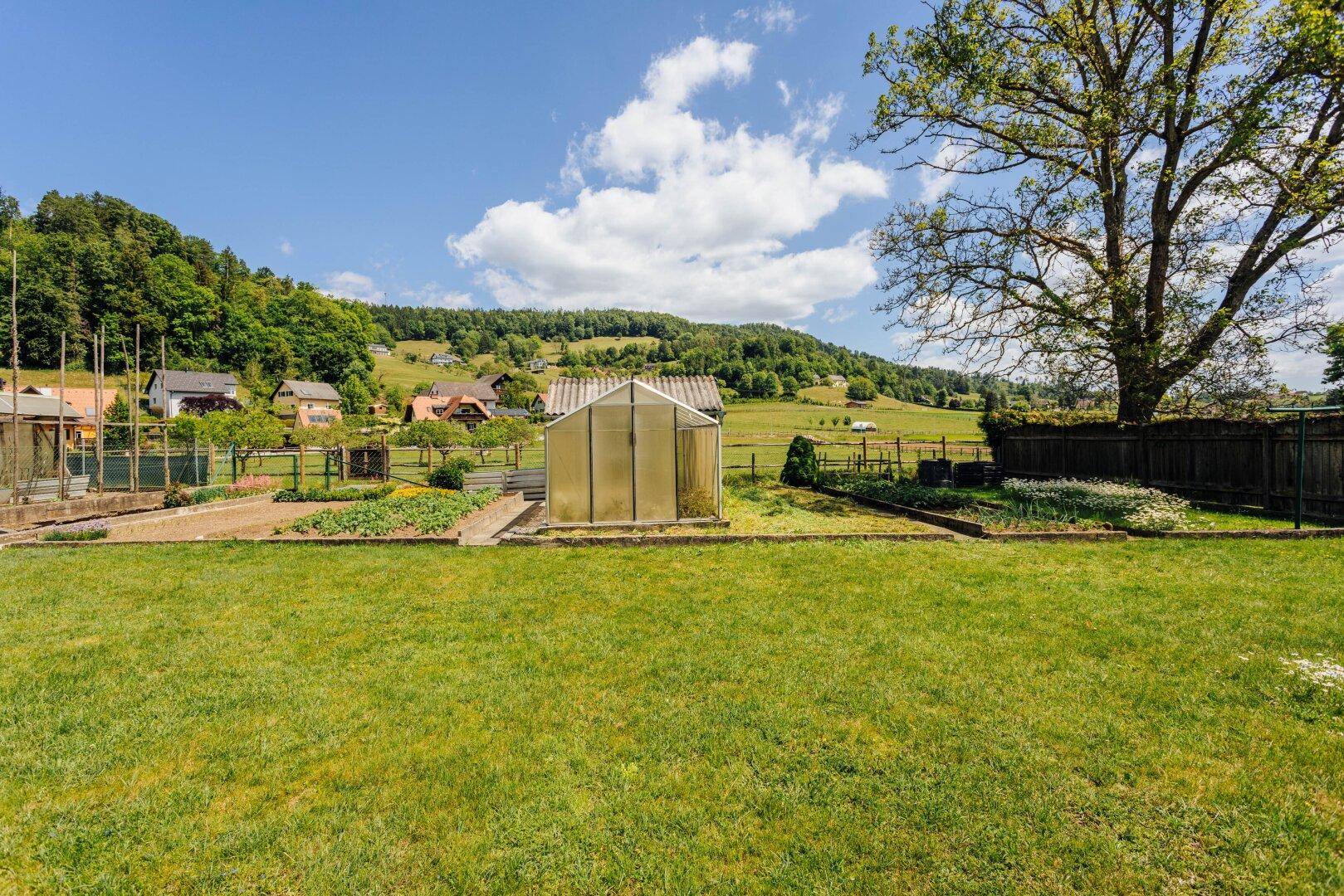 Garten mit einem Gewächshaus im Mittelpunkt, umgeben von Rasen und sanften Hügeln.