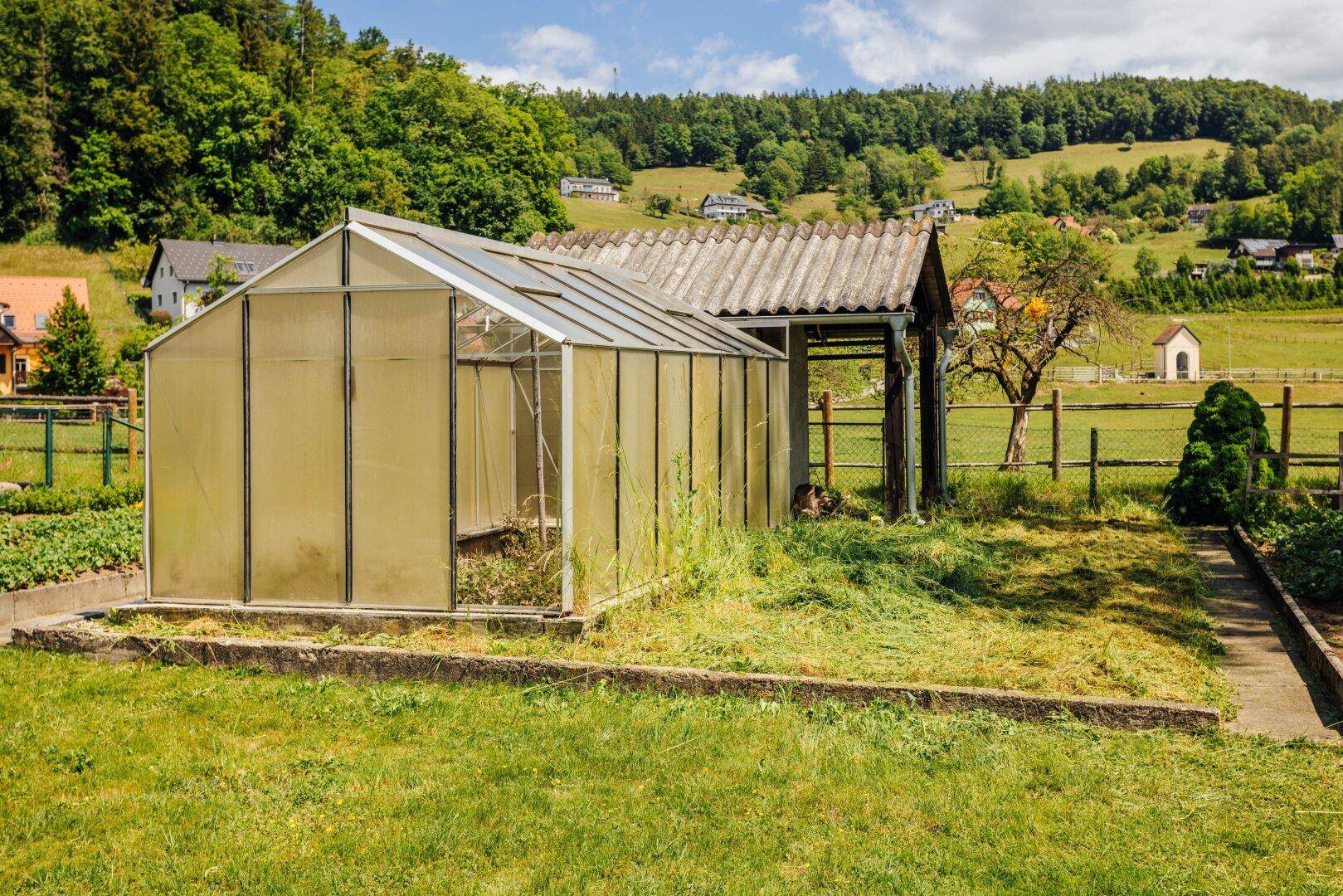 Gewächshaus und Schuppen in einem Garten mit Anbauflächen und weitem Blick.