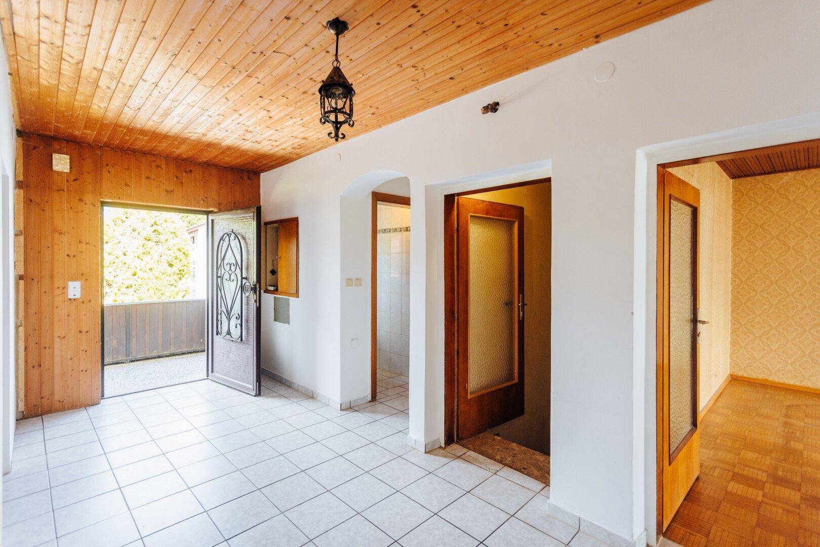 Heller Eingangsbereich mit Fliesenboden, Holzdecke und Zugang zu einem Außenbereich, mit traditioneller Tür.