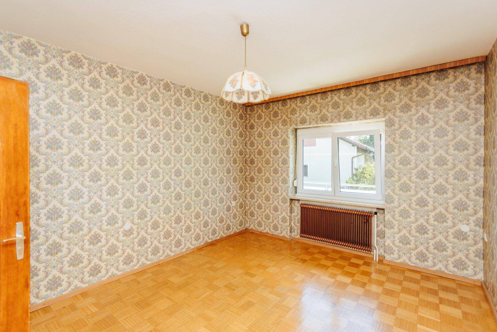 Helles Schlafzimmer mit Parkettboden, gemusterter Tapete und Fenster, ideal für individuelle Gestaltung.