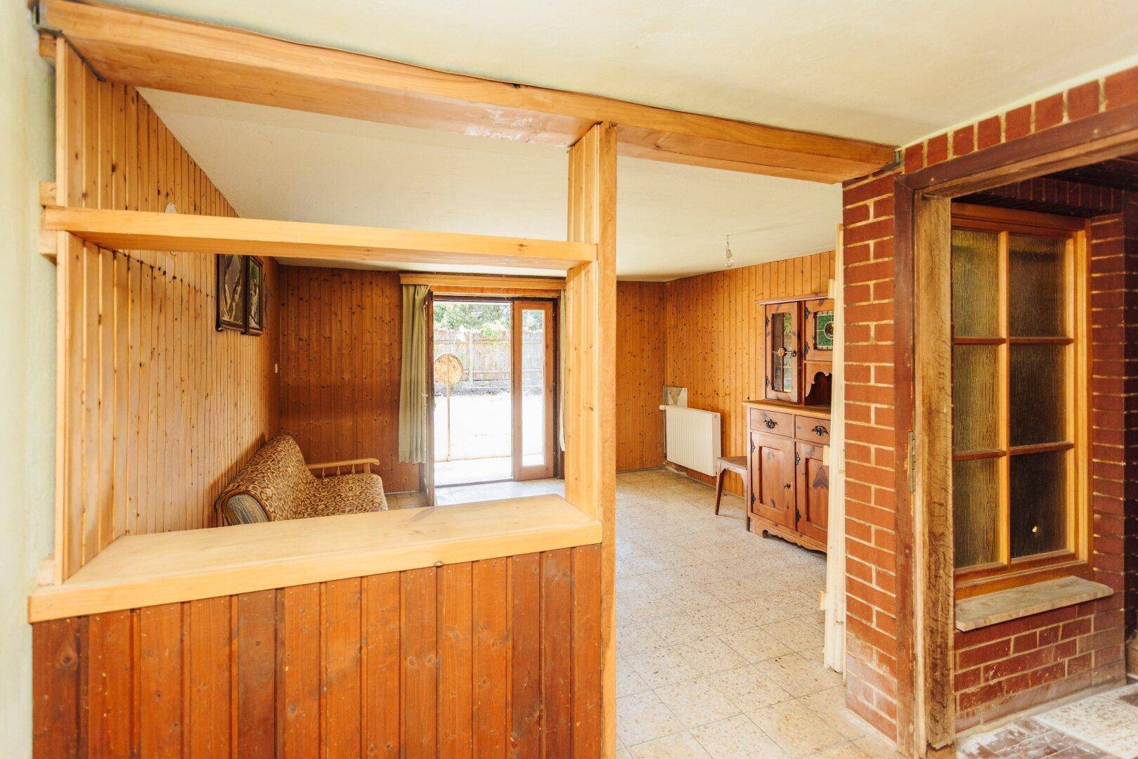 Rustikaler Wohnbereich mit Holzvertäfelung, Fliesenboden und Zugang zum Garten, mit Thekenbereich.