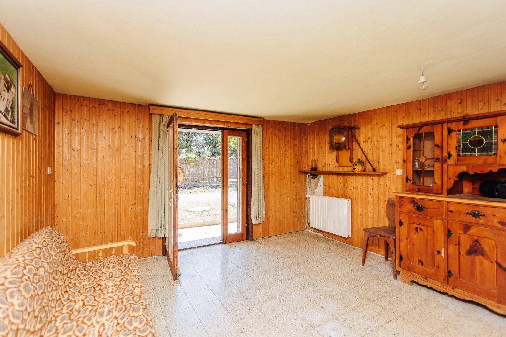 Gemütlicher Wohnraum mit Holzvertäfelung, Fliesenboden und direktem Zugang zum Garten.