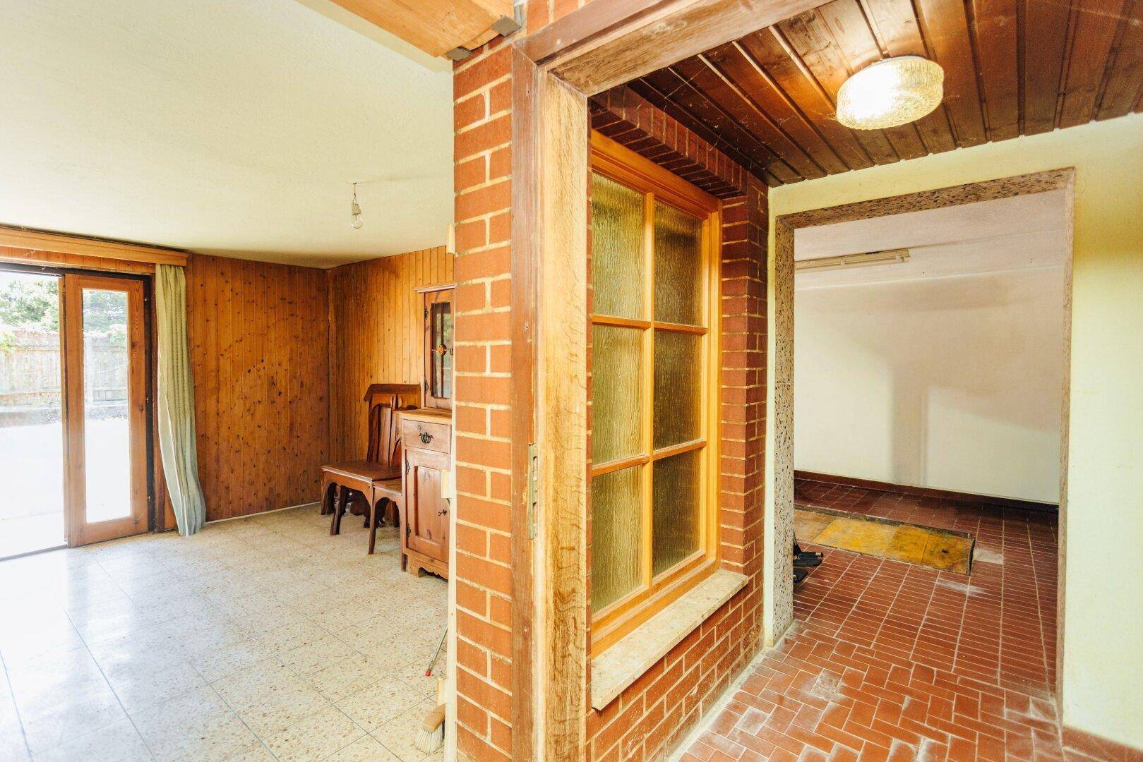Eingangsbereich mit Ziegelwand, Holzvertäfelung und Fenster, führt in den Wohnbereich.