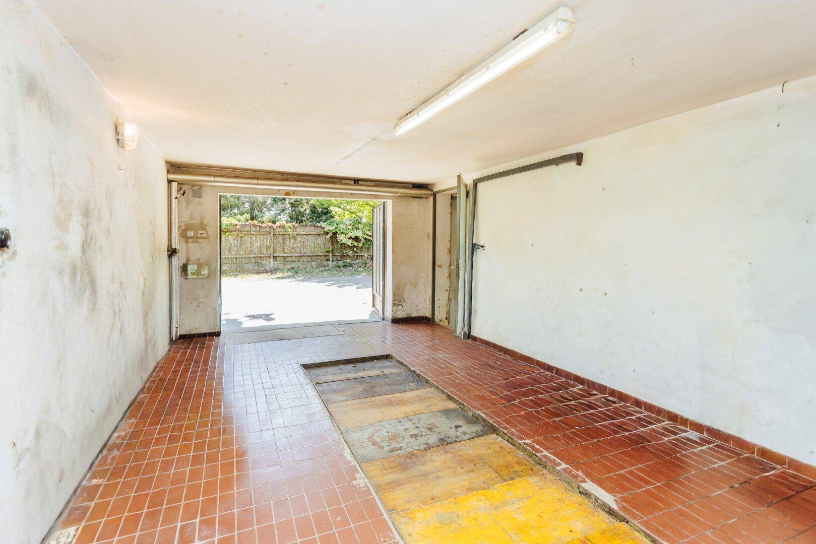 Geräumige Garage mit Fliesenboden und Inspektionsgrube, mit direktem Zugang zum Außenbereich.
