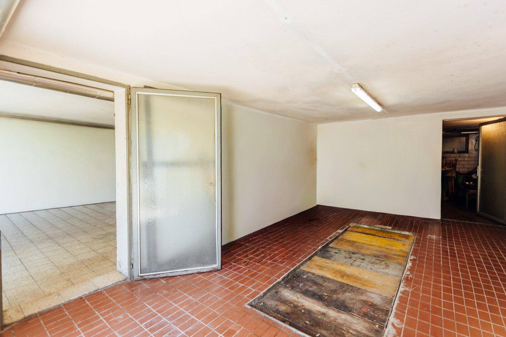 Garage mit Fliesenboden und Inspektionsgrube, bietet Zugang zu weiteren Räumen.