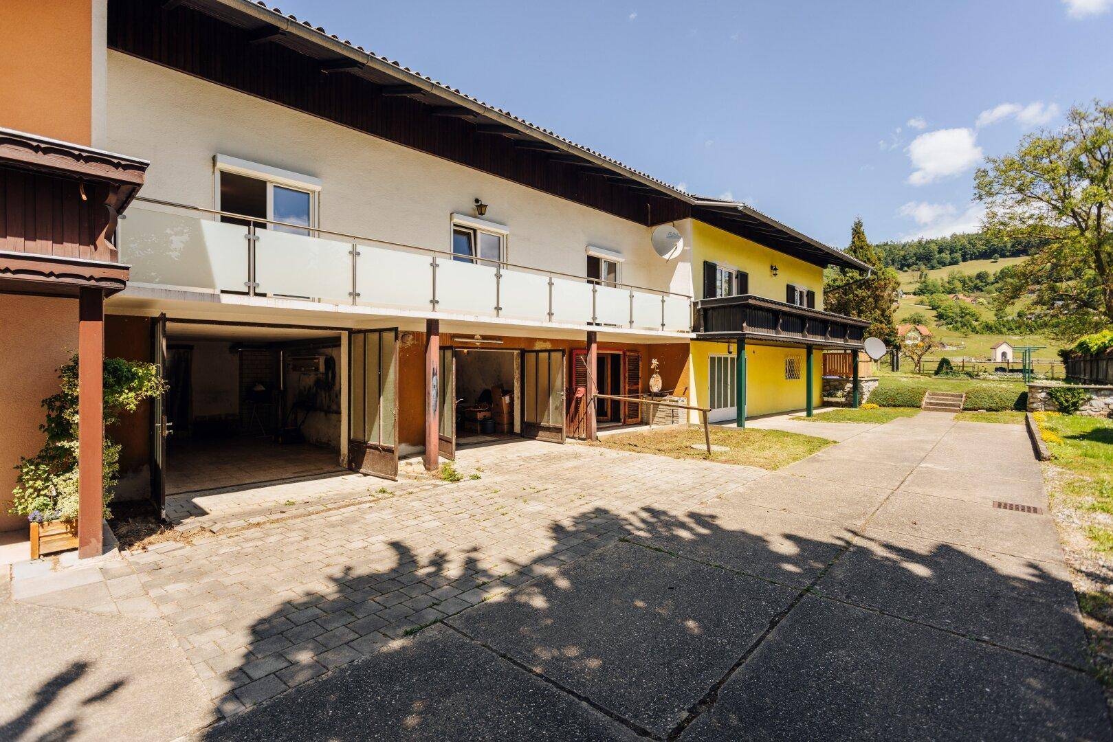 Ansicht des Hauses von außen mit Garagenzugang, Balkon und grüner Umgebung.