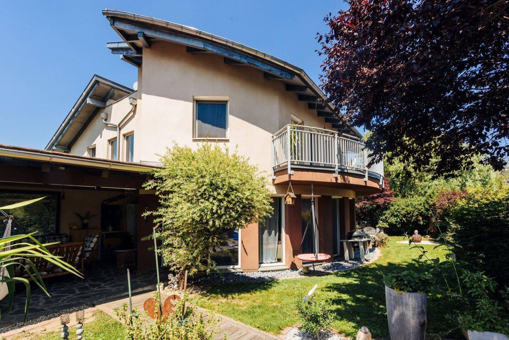 Ansicht des Hauses von der Gartenseite mit Balkon, Terrasse und üppiger Bepflanzung.