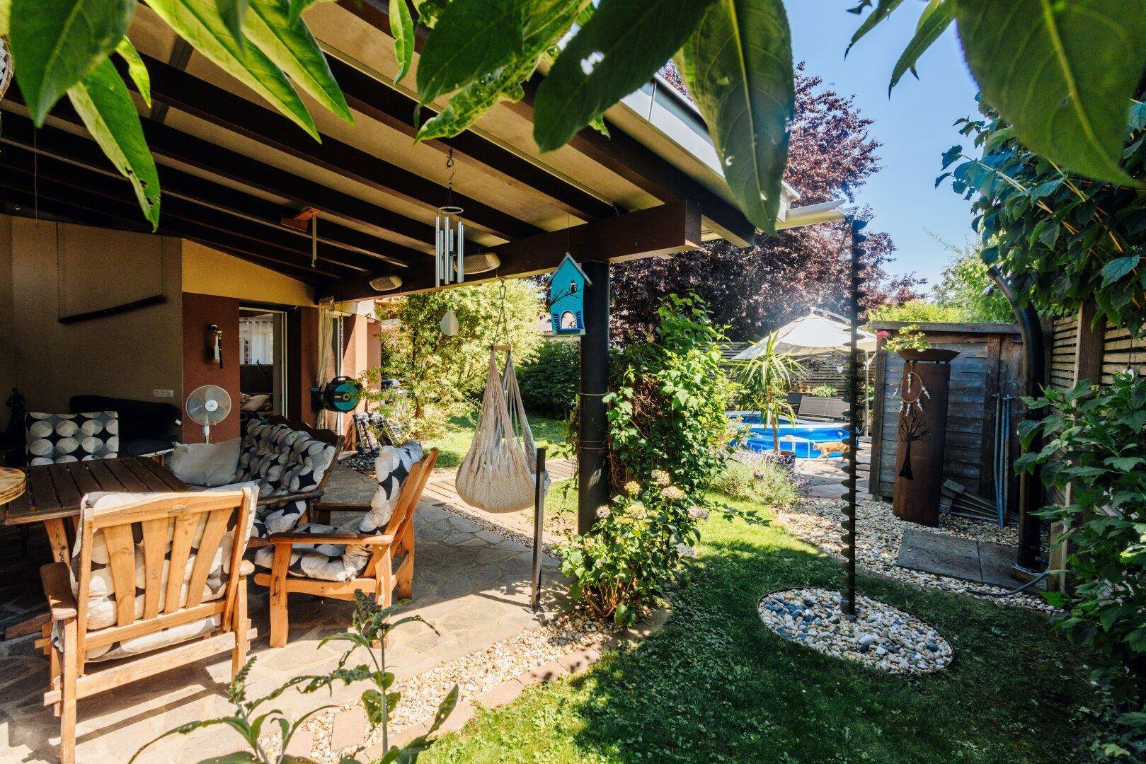 Überdachte Terrasse mit Holzmöbeln und Blick auf den Garten mit Poolbereich.