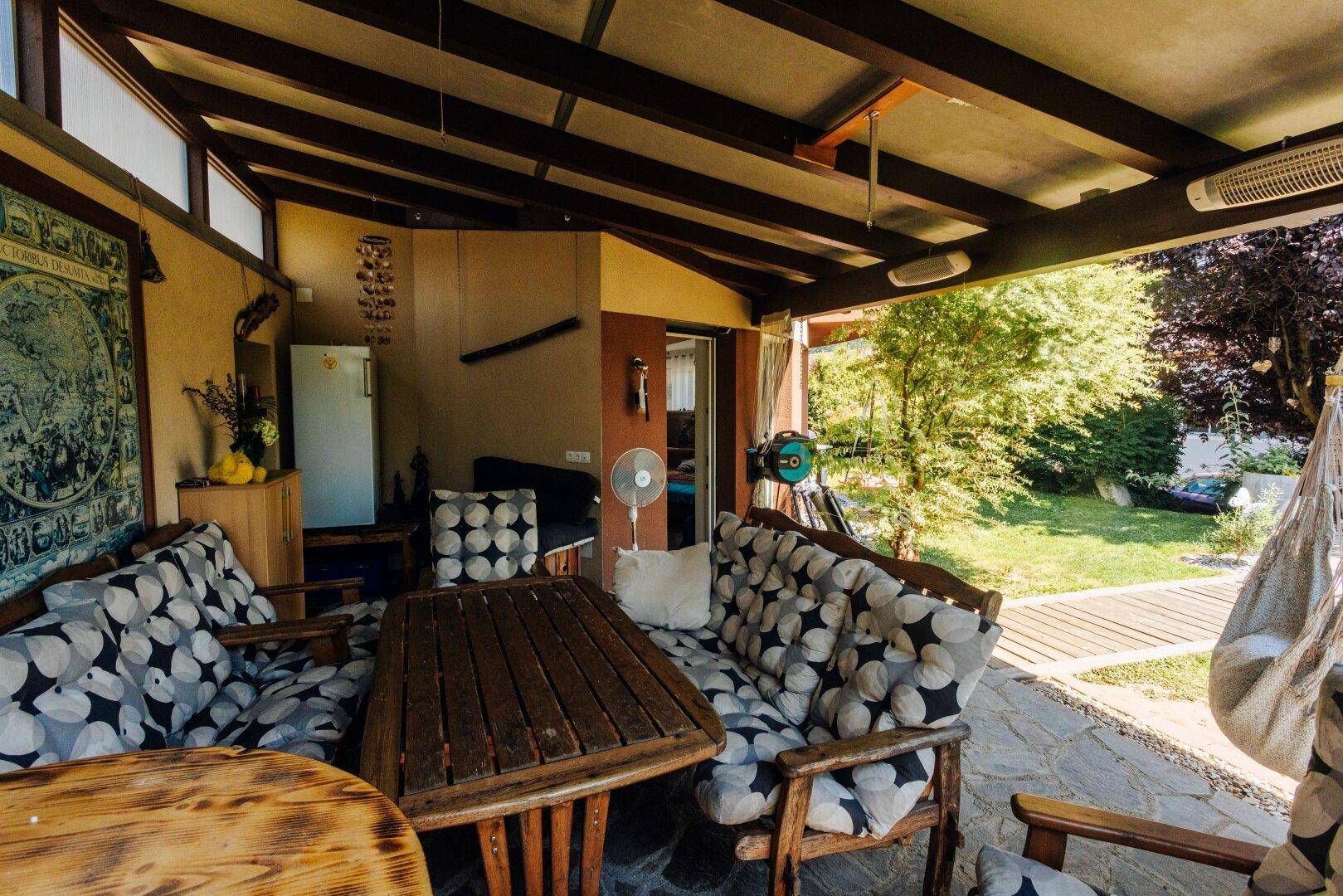 Gemütliche überdachte Terrasse mit bequemen Sitzmöbeln und rustikalem Holztisch.