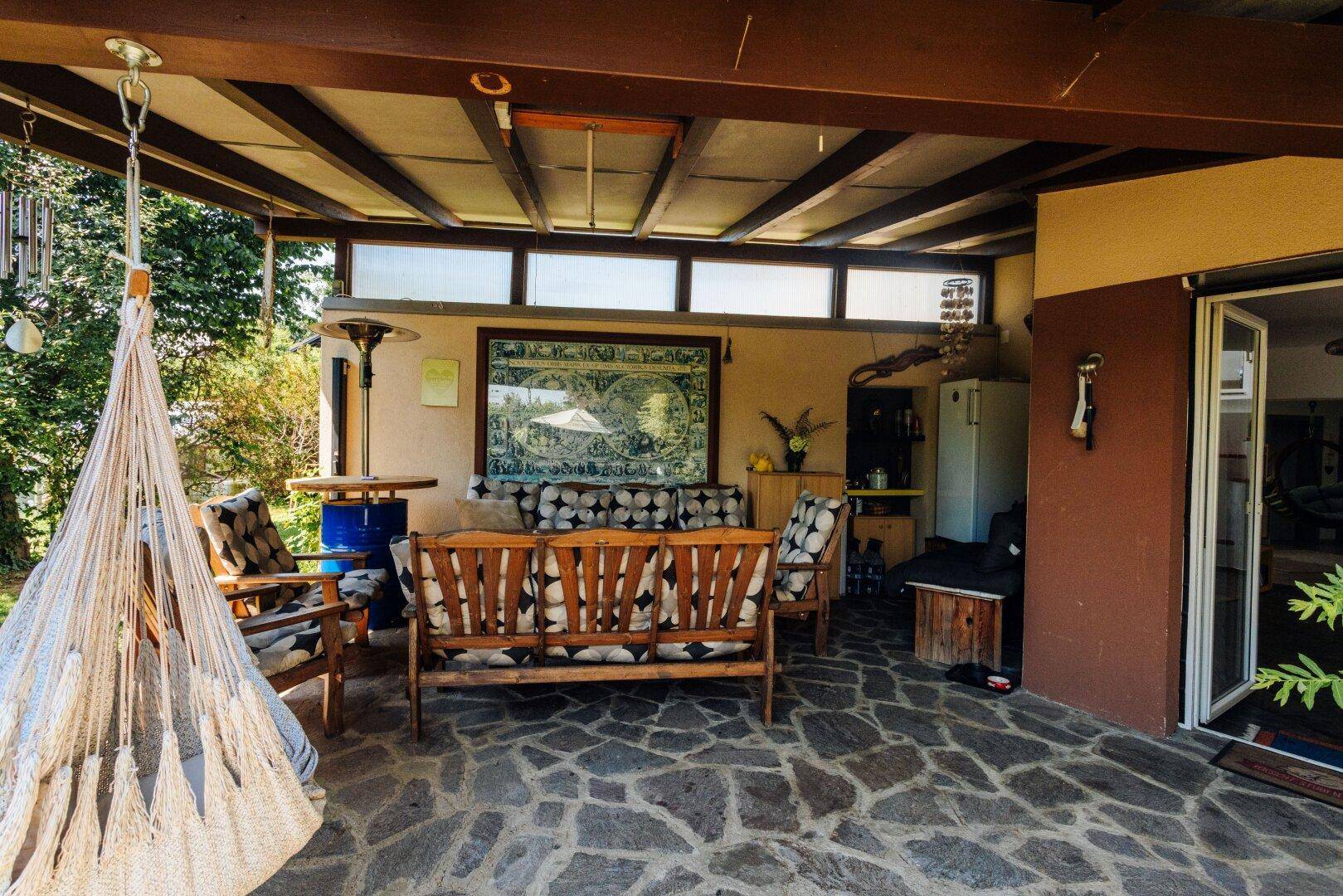 Geräumige überdachte Terrasse mit Steinboden, Hängesessel und Zugang zum Haus.