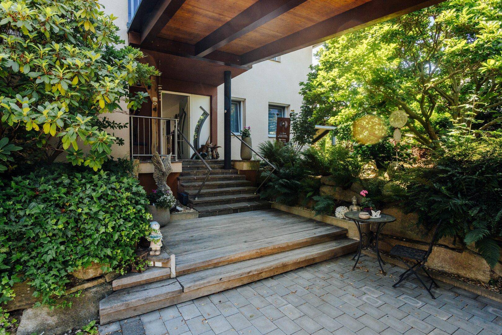Eingangsbereich mit Holzstufen, kleiner gepflasterter Terrasse und dekorativen Pflanzen.