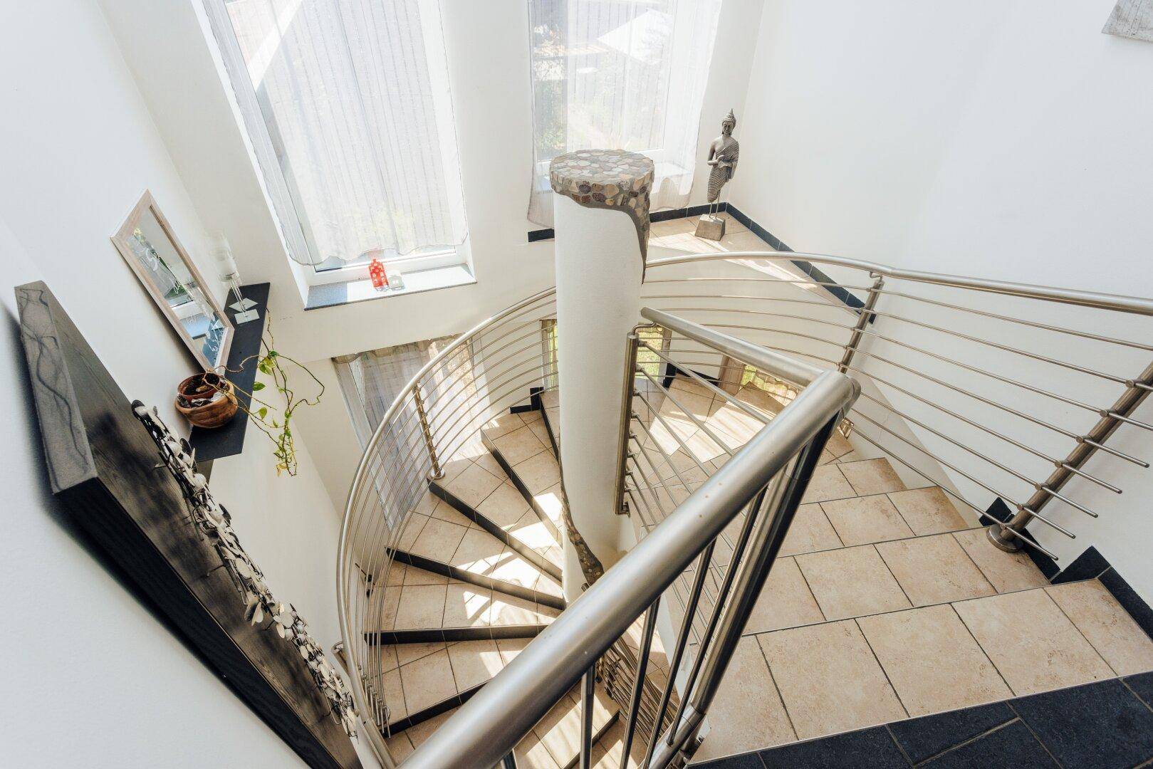 Elegante Wendeltreppe mit Edelstahlgeländer und gefliestem Boden.