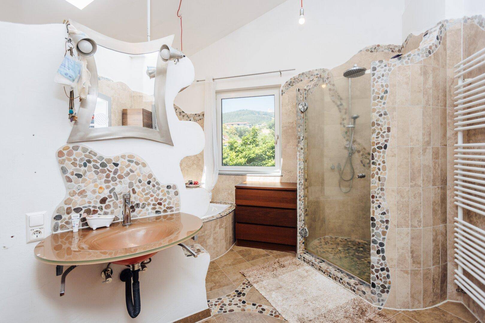 Modernes Badezimmer mit Dusche, Waschbecken und dekorativen Kieselementen.