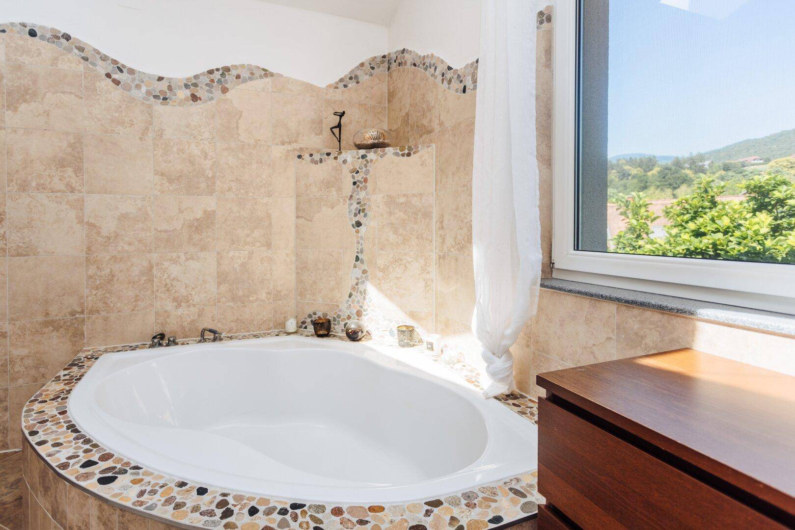 Geräumiges Badezimmer mit Badewanne, Fenster und Blick ins Grüne.