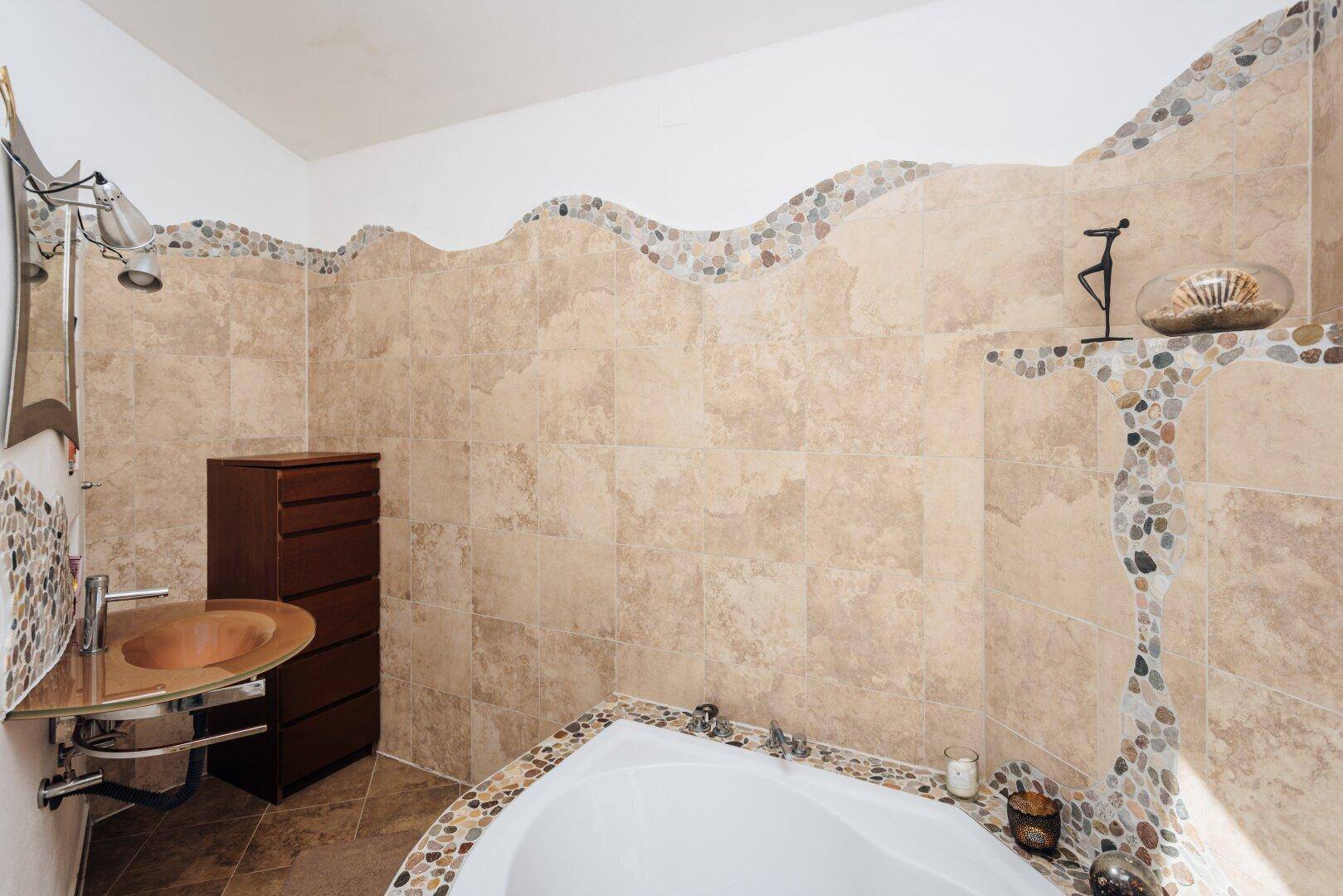Modernes Badezimmer mit Badewanne, Waschbecken und dekorativen Kiesdetails.