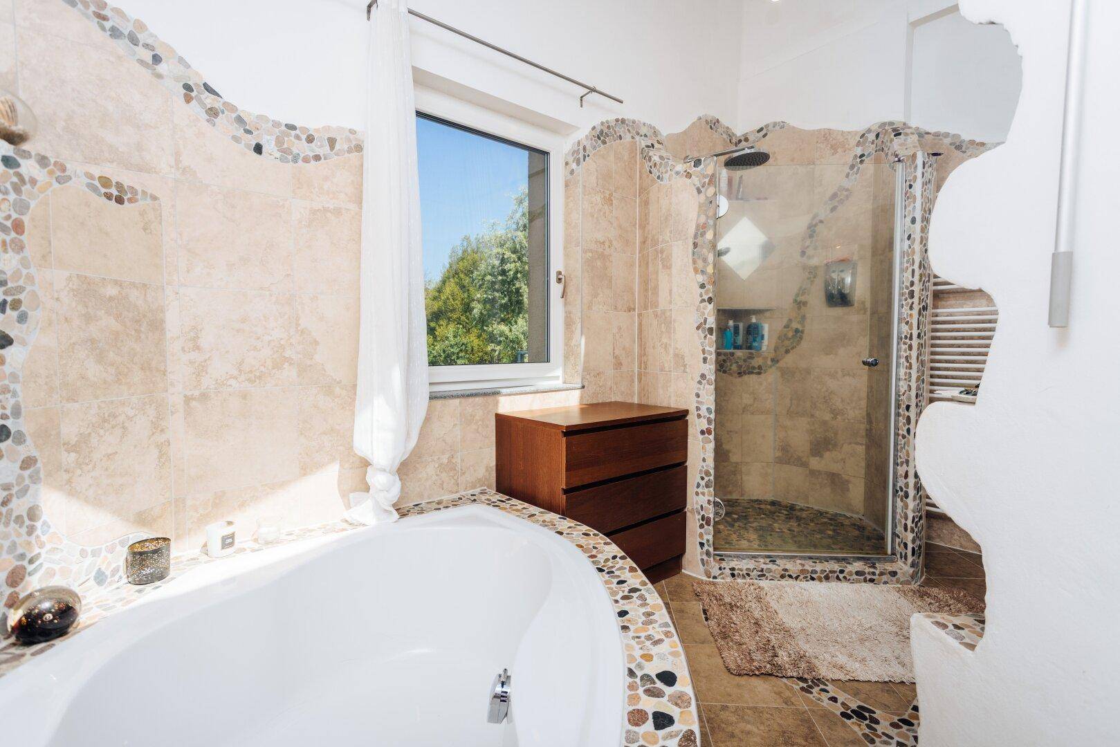 Helles Badezimmer mit Badewanne, Dusche und Fenster mit Ausblick.