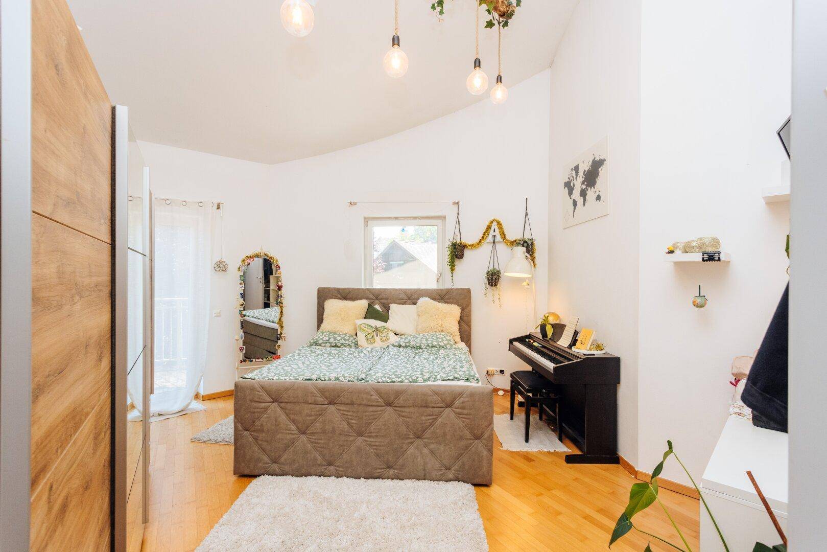 Gemütliches Schlafzimmer mit Holzboden, hohen Decken und Fenster mit Blick ins Grüne.