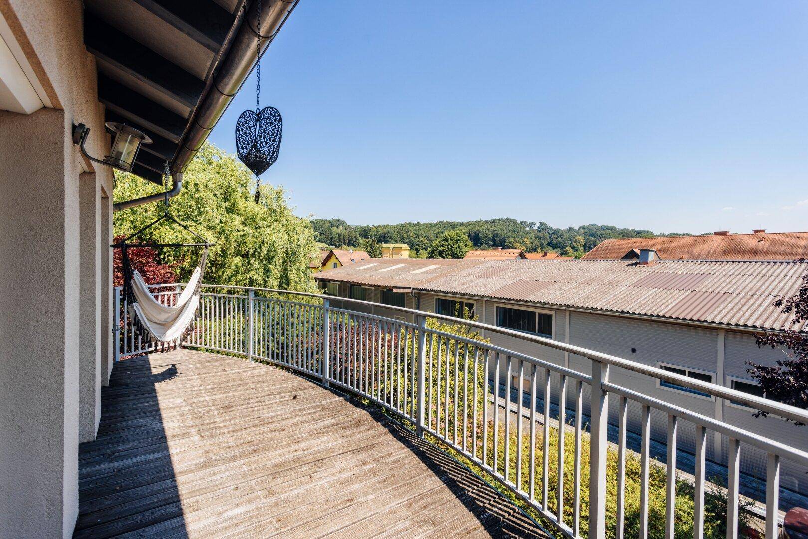 Großer Balkon mit Holzboden und Metallgeländer bietet weiten Blick ins Grüne.
