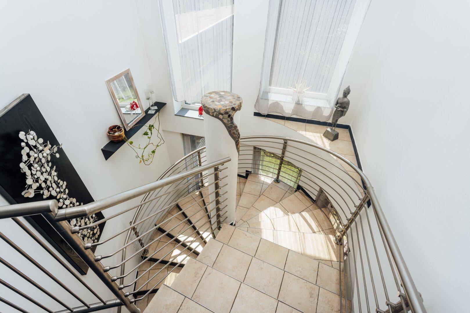 Wendeltreppe mit Metallgeländer und Fliesenboden, die verschiedene Ebenen verbindet.