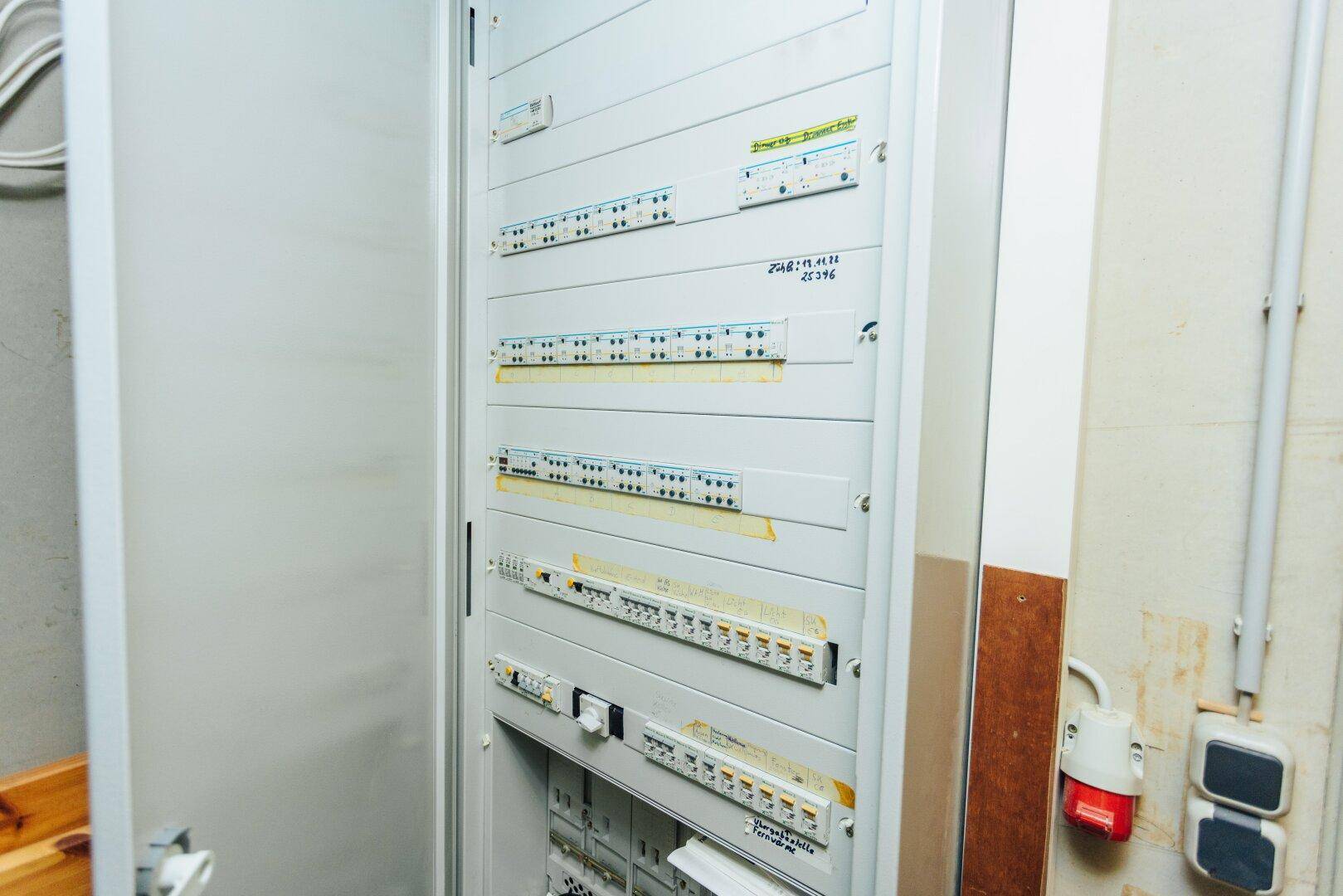 Offener Sicherungskasten mit vielen Schaltern und Verkabelungen in einem Technikraum.