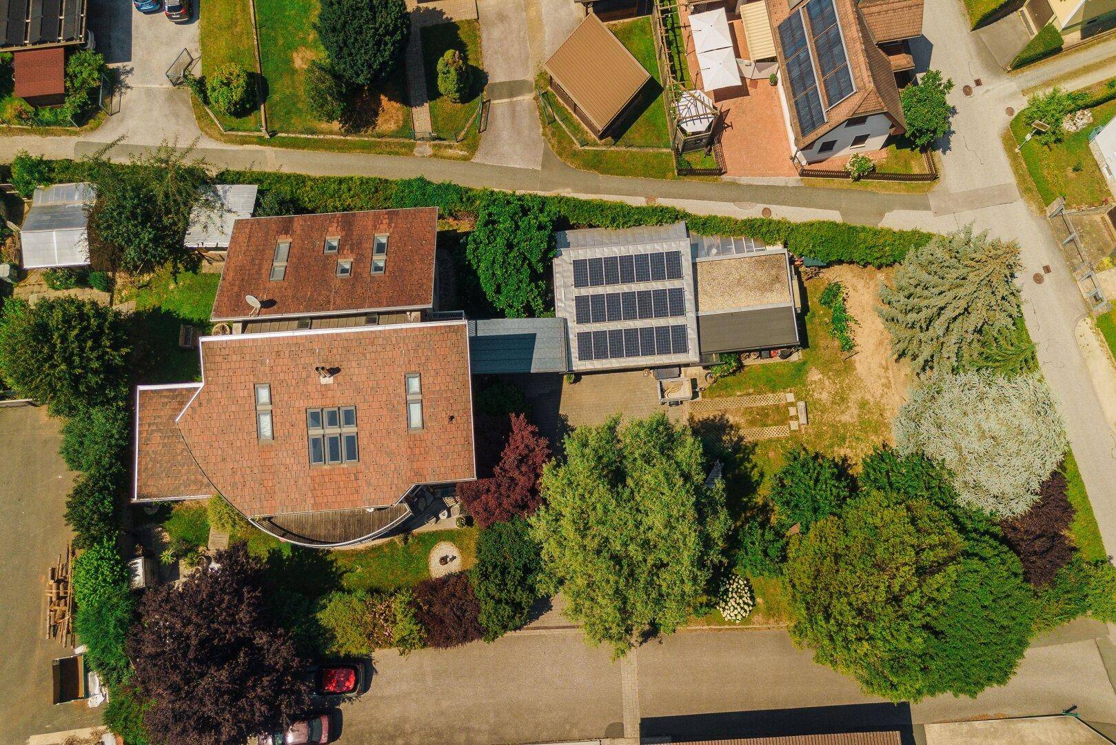 Luftaufnahme eines Anwesens mit mehreren Gebäuden, Photovoltaikanlagen und großem Gartenbereich.
