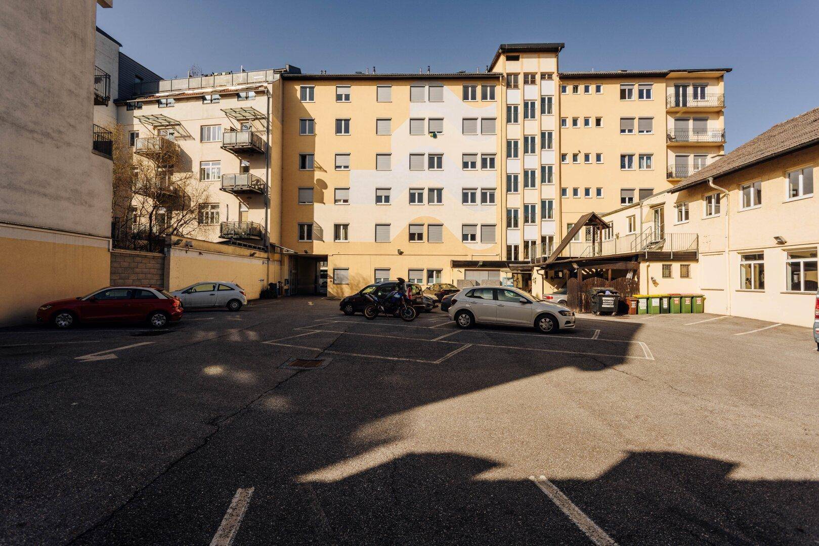 Großer Außenparkplatz mit Autos vor einem mehrstöckigen Gebäude mit vielen Fenstern.