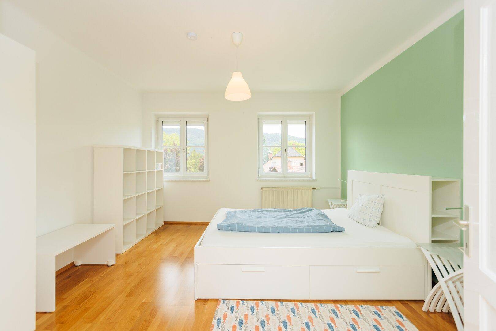 Geräumiges Schlafzimmer mit Holzboden, einem großen Bett und einer hellgrünen Akzentwand.