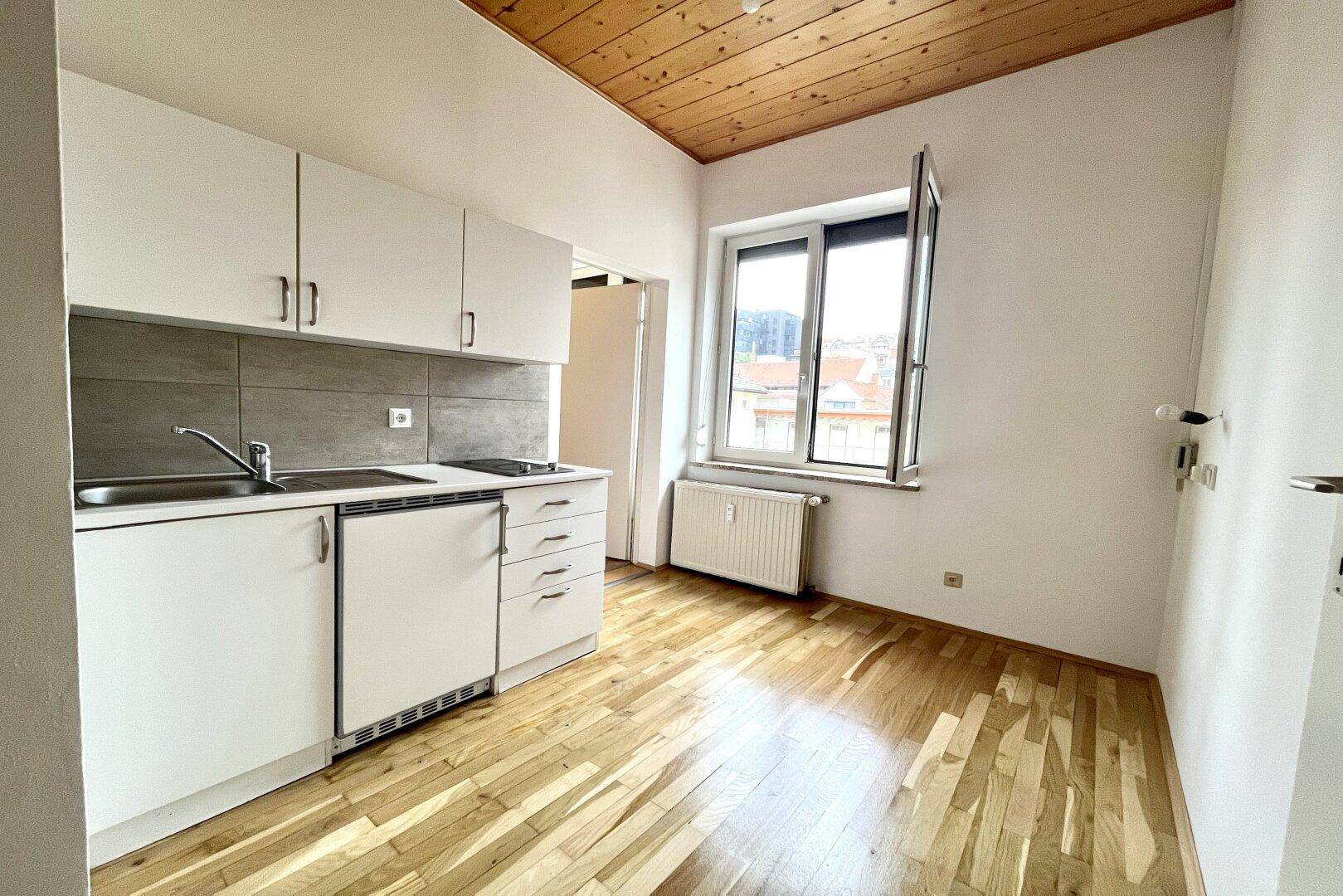 Funktionale Küchenzeile mit weißen Schränken, Spüle und einem Fenster, unter einer Holzbalkendecke.