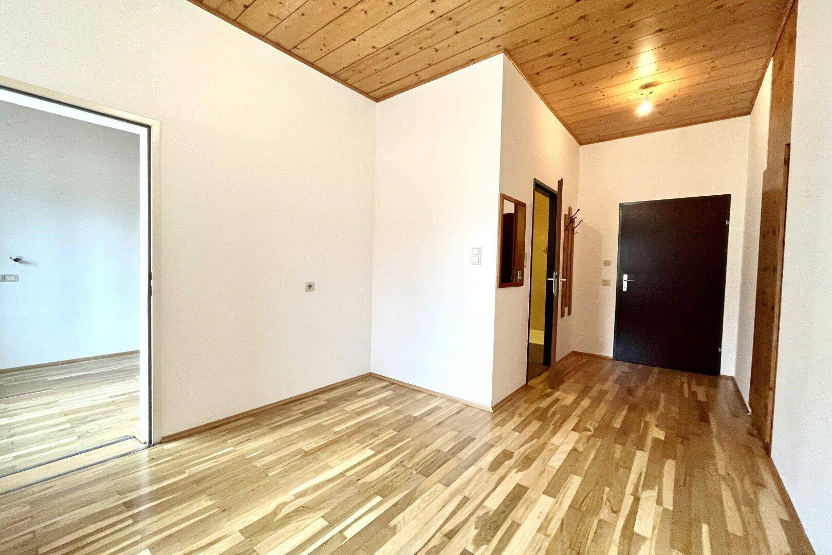 Geräumiger Flur mit Holzbalkendecke, Parkettboden und einem Spiegel, der zum Eingangsbereich führt.