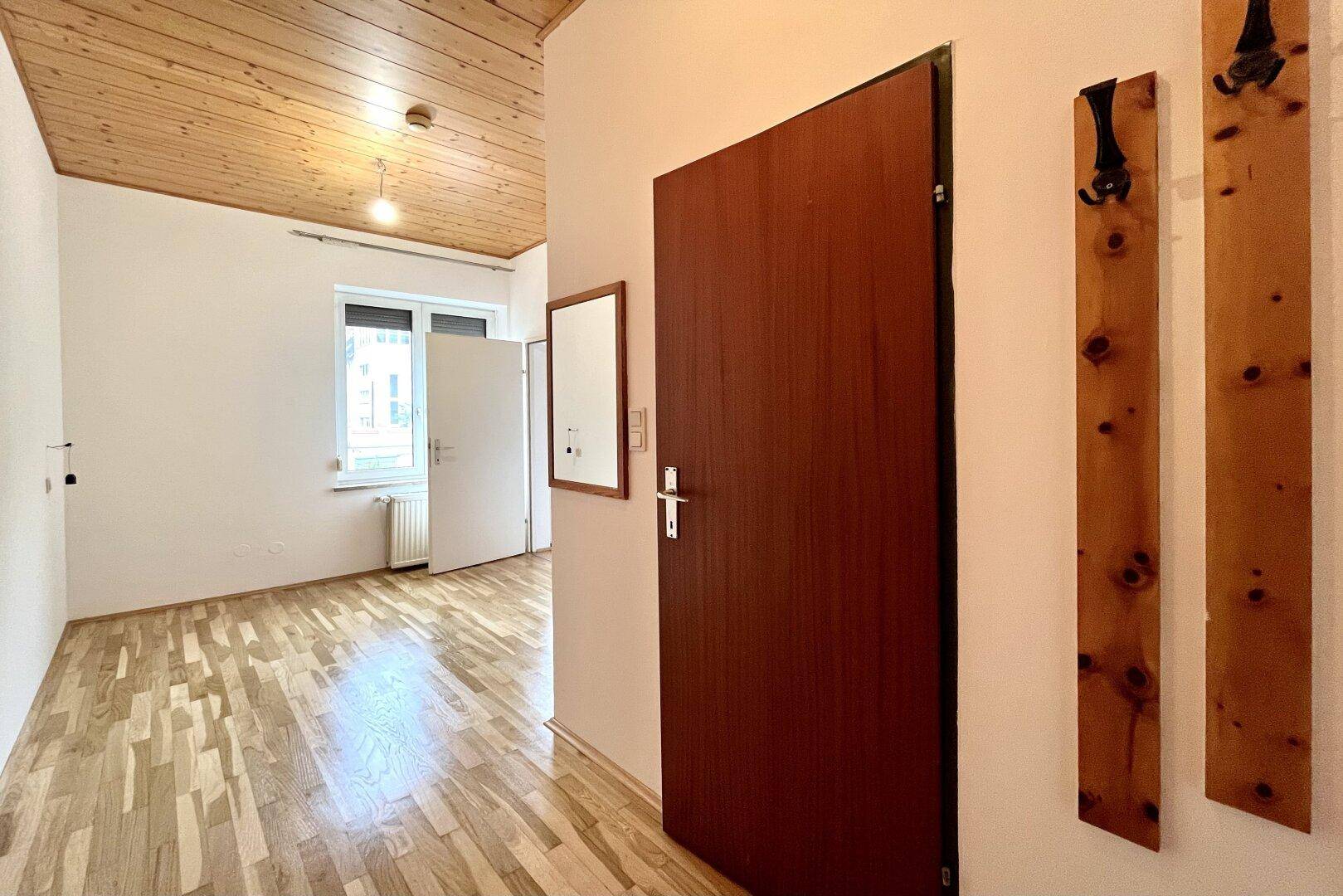 Eingangsbereich mit Holzbalkendecke, Parkettboden und einer Garderobe, die zum Haupteingang führt.