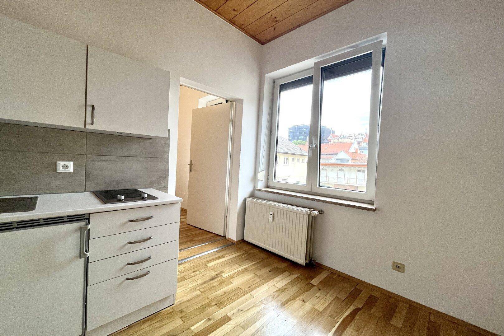 Blick aus dem Zimmer auf die Küchenzeile, mit Heizkörper unter dem Fenster und Holzbalkendecke.