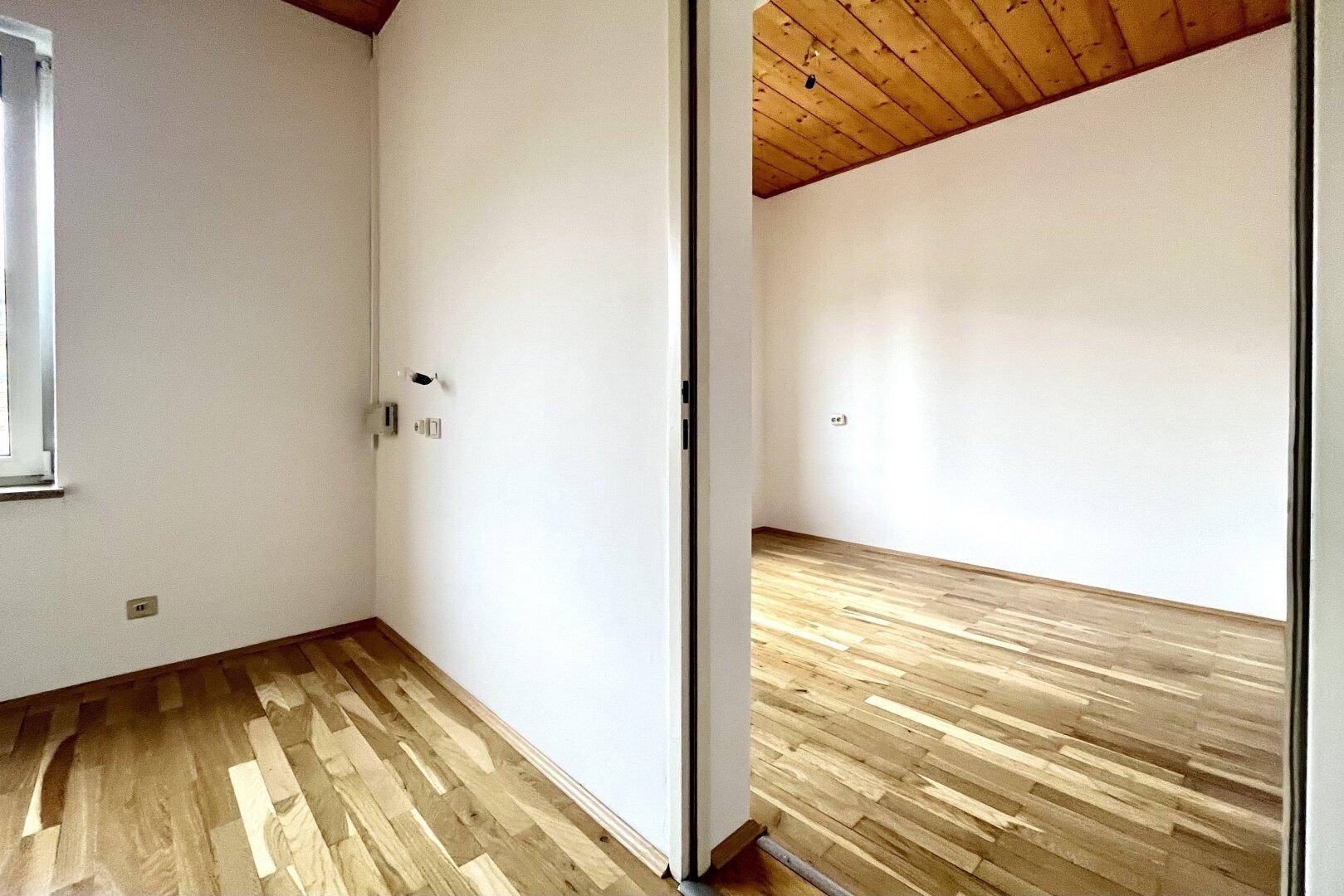 Offener Durchgang zwischen zwei hellen Räumen mit Holzbalkendecke und Parkettboden.